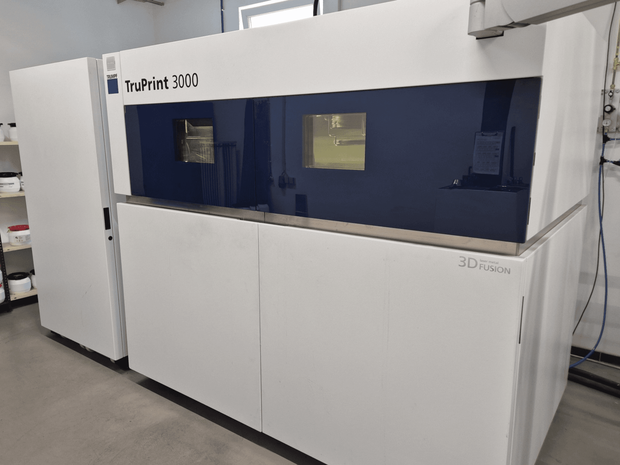 "TruPrint 3000" metalinis 3D spausdintuvas iš priekio - mėlynos spalvos plokštelėmis ir lazerinės sintezės technologija.