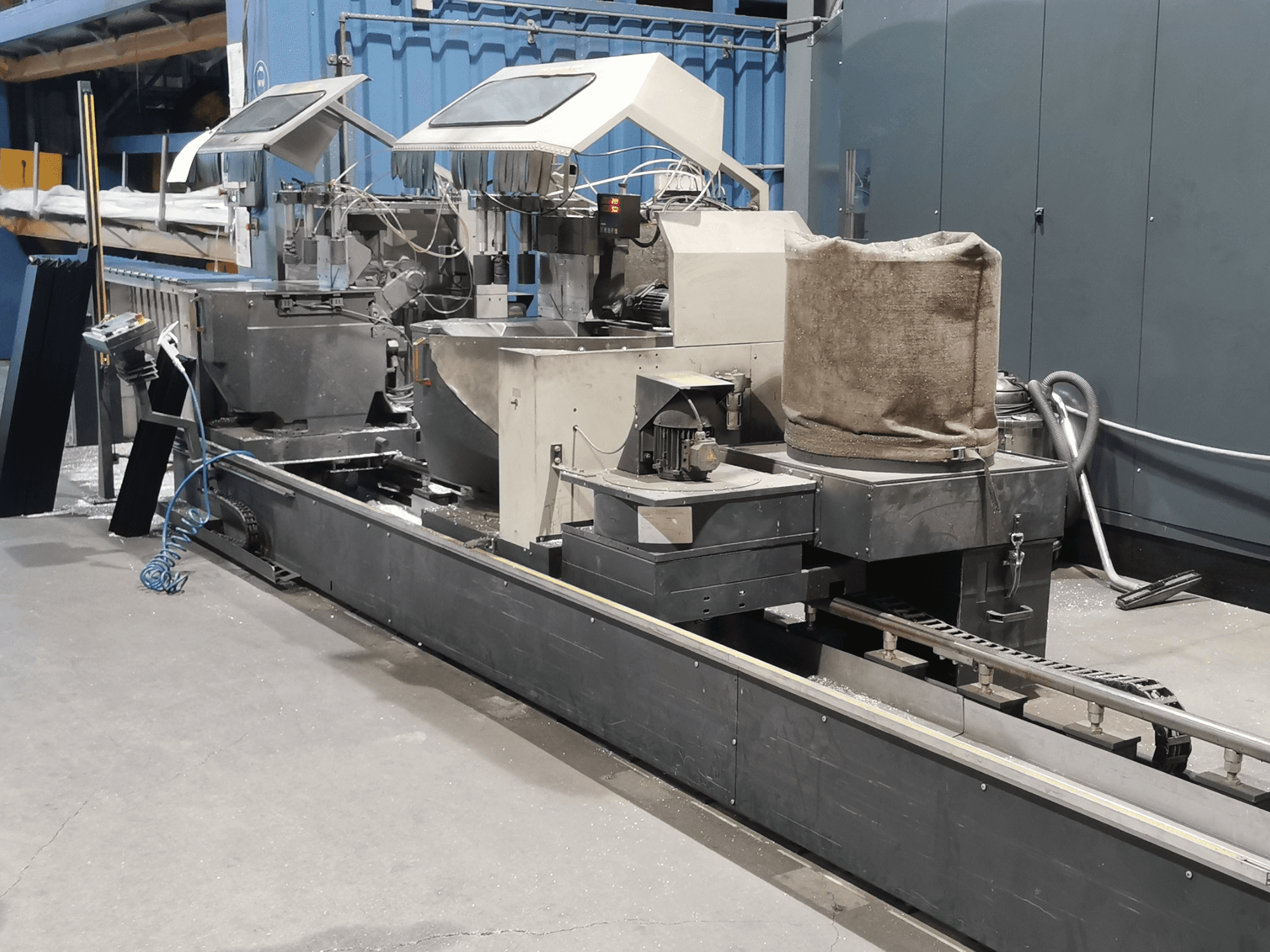 Pramoninė apdirbimo mašina, žiūrint iš šono, su bunkeriais, konvejerio juosta ir valdymo pultu gamykloje.