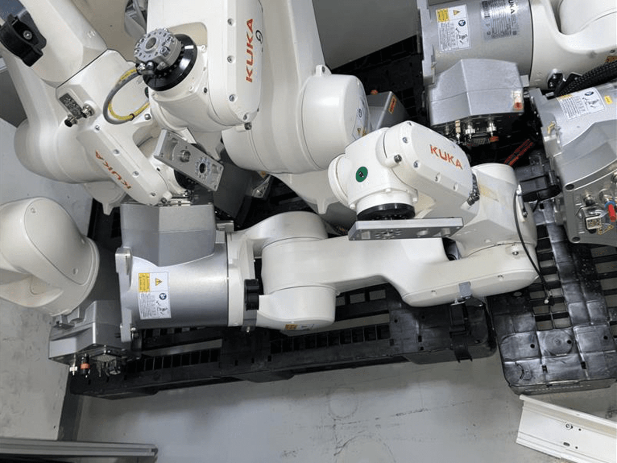 KUKA KR 6 R900 CR roboto rankos vaizdas iš viršaus, su keliais sąnariais ir varikliais, pritvirtinta ant juodo pagrindo su laidais.