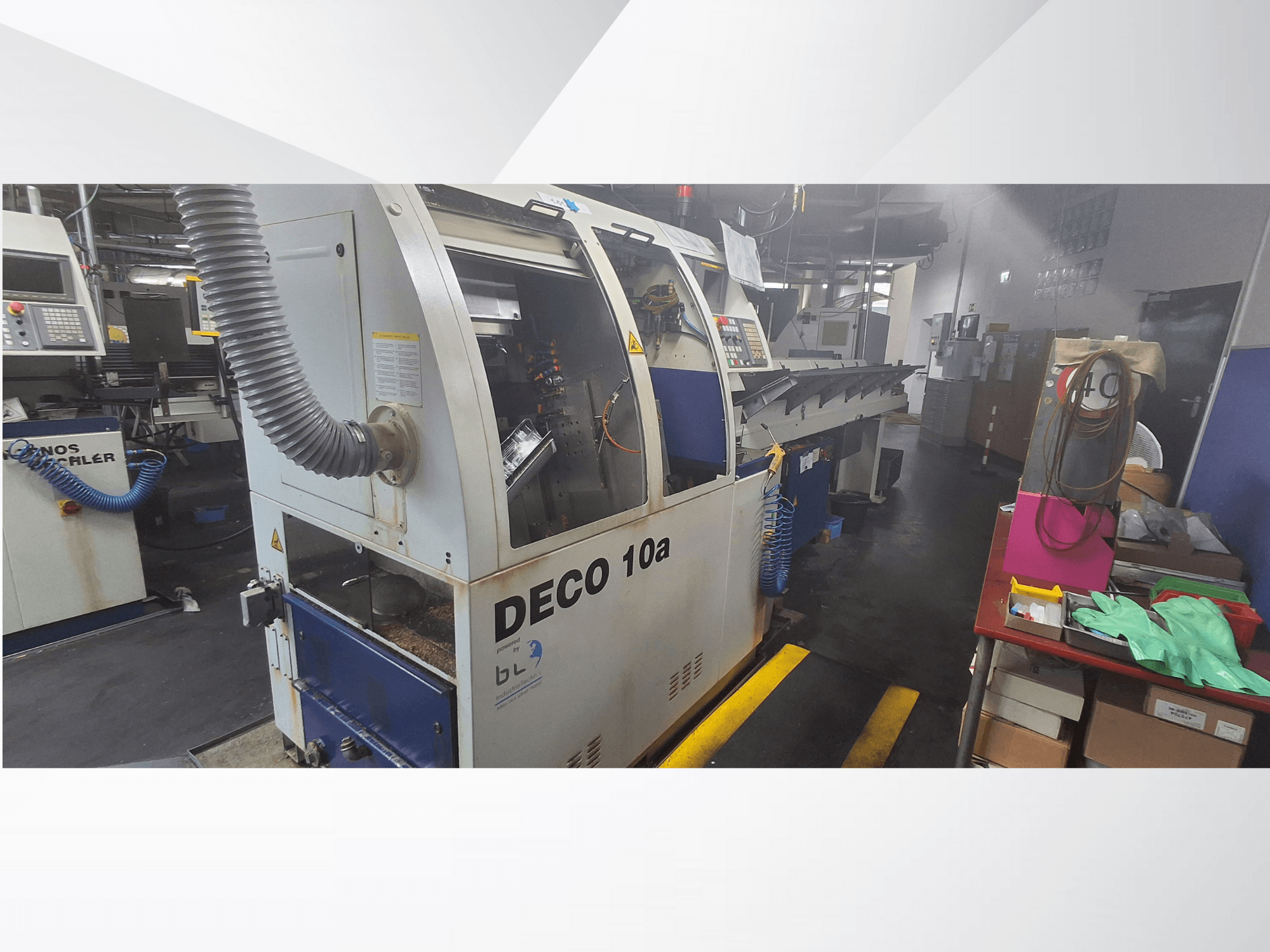 DECO 10a CNC staklės dirbtuvėse, vaizdas iš priekio; su valdymo skydeliu ir dulkių ištraukimo sistema, šalia - darbo stalas.