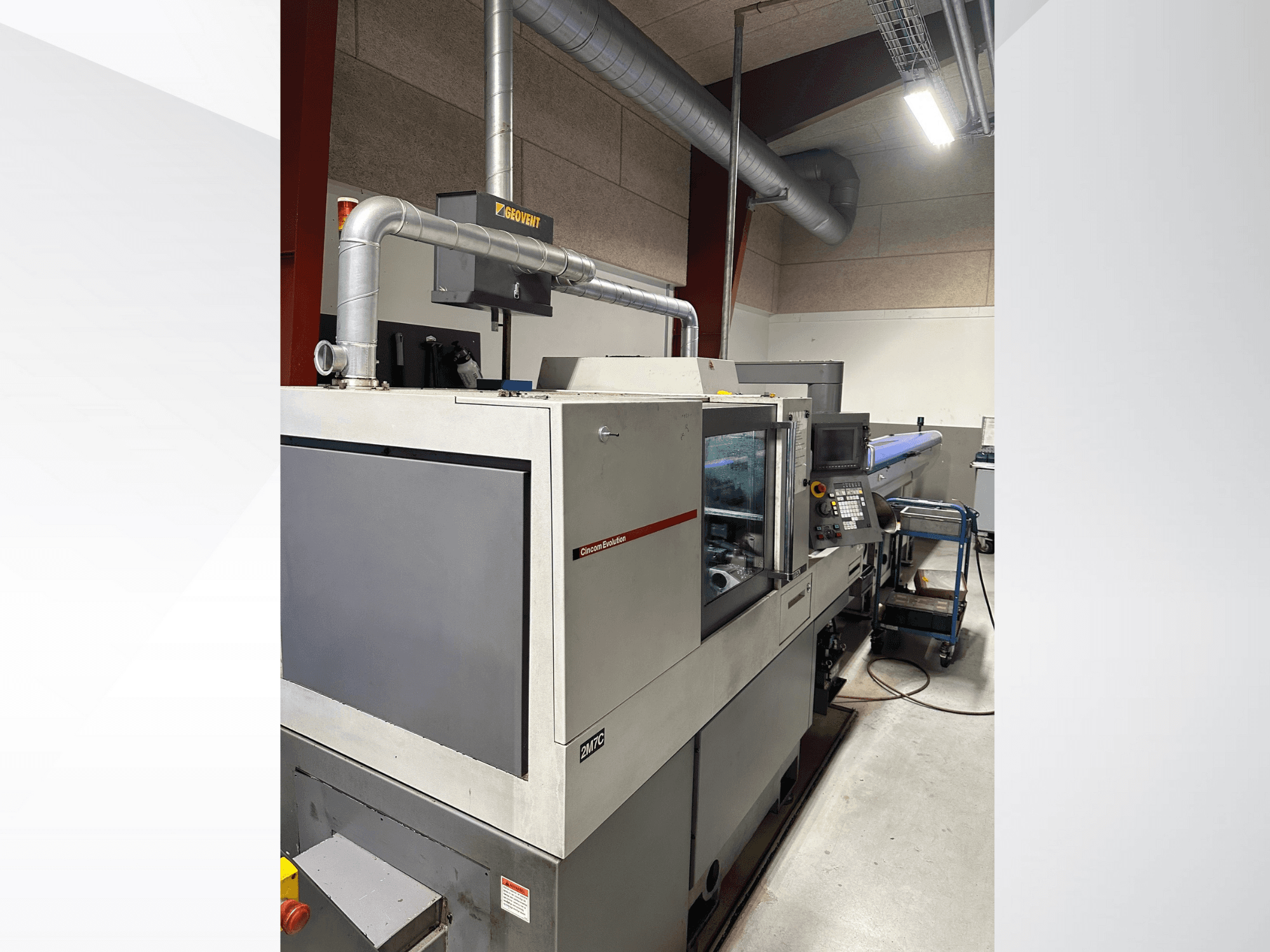 MVC prekės ženklo pramoninės mašinos, vaizdas iš šono, matomas valdymo skydelis ir ortakiai, įrengtos gamyklos aplinkoje.