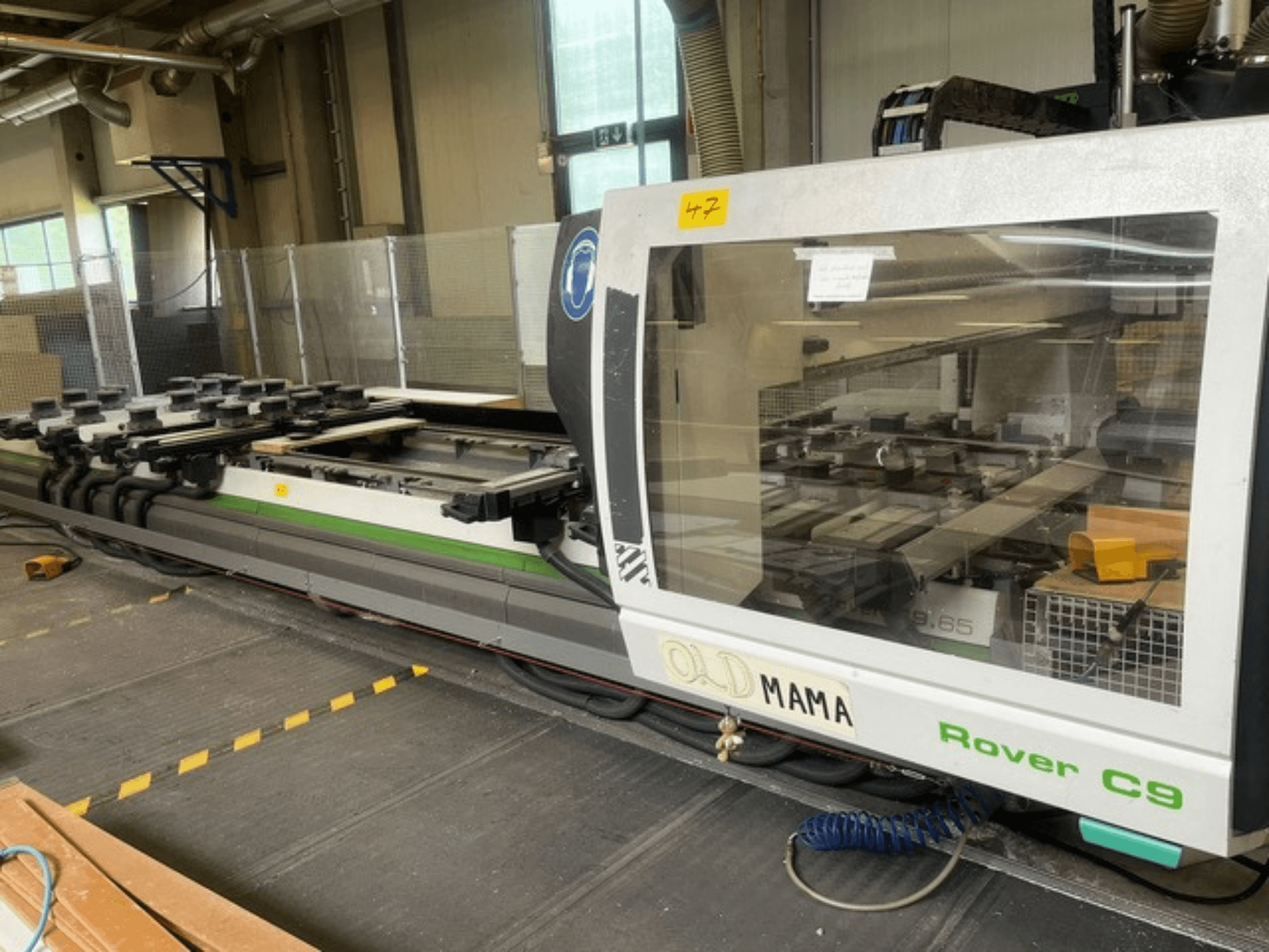 BIESSE Rover C 9.65 CNC maršrutizatorius dirbtuvėse, šoninis vaizdas, rodantis valdymo skydelį ir stalą su spaustukais.