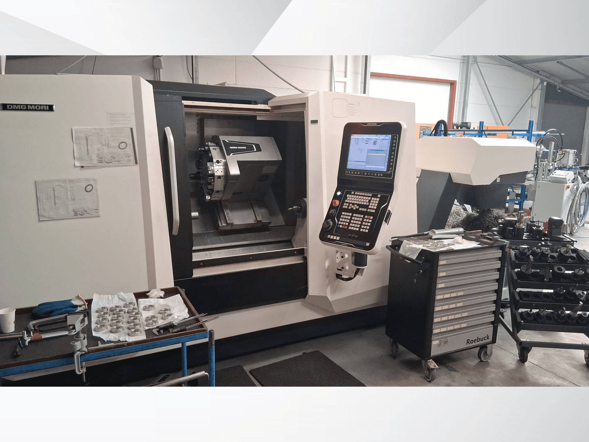 DMG MORI CLX450 horizontaliosios tekinimo staklės iš priekio - valdymo skydelis, darbo zona, įrankiai ir metalinės detalės.