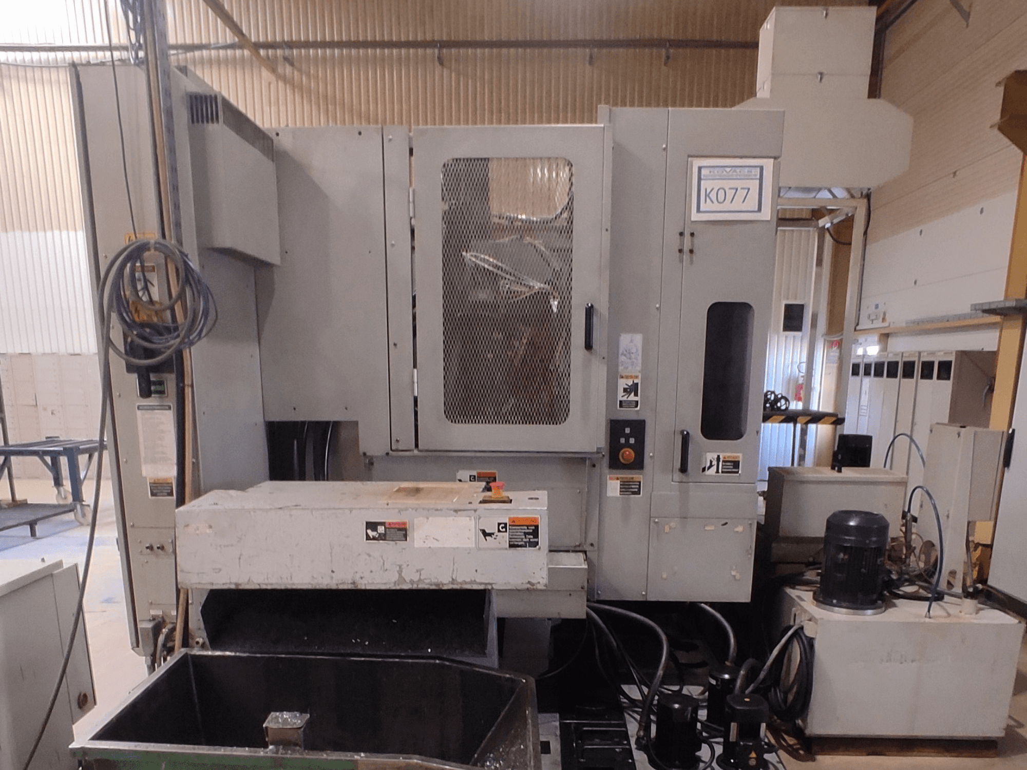 Pilkos pramoninės CNC staklės su dideliu darbo stalu, vaizdas iš šono, su valdymo skydeliu ir aušinimo skysčio rezervuaru, K077 modelis.