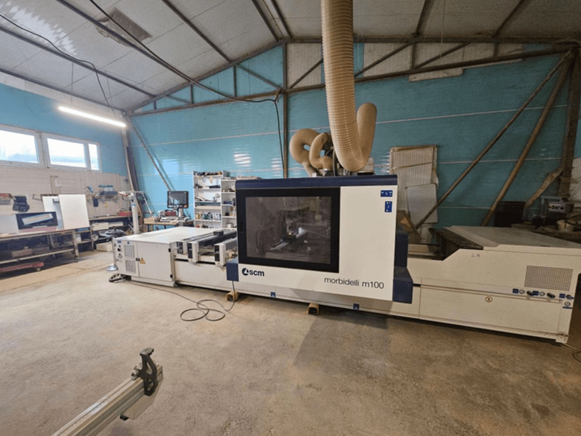 SCM MORBIDELLI M 100 CNC apdirbimo centras dirbtuvėse, vaizdas iš priekio su dulkių surinkimo sistema ir aplinkine darbo vietos įranga.