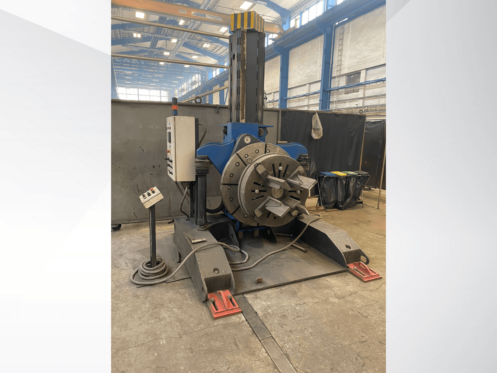 Mėlynos pramoninės tekinimo staklės su apvalia besisukančia galvute ir valdymo skydeliu, vaizdas iš šono, dirbtuvių aplinka.