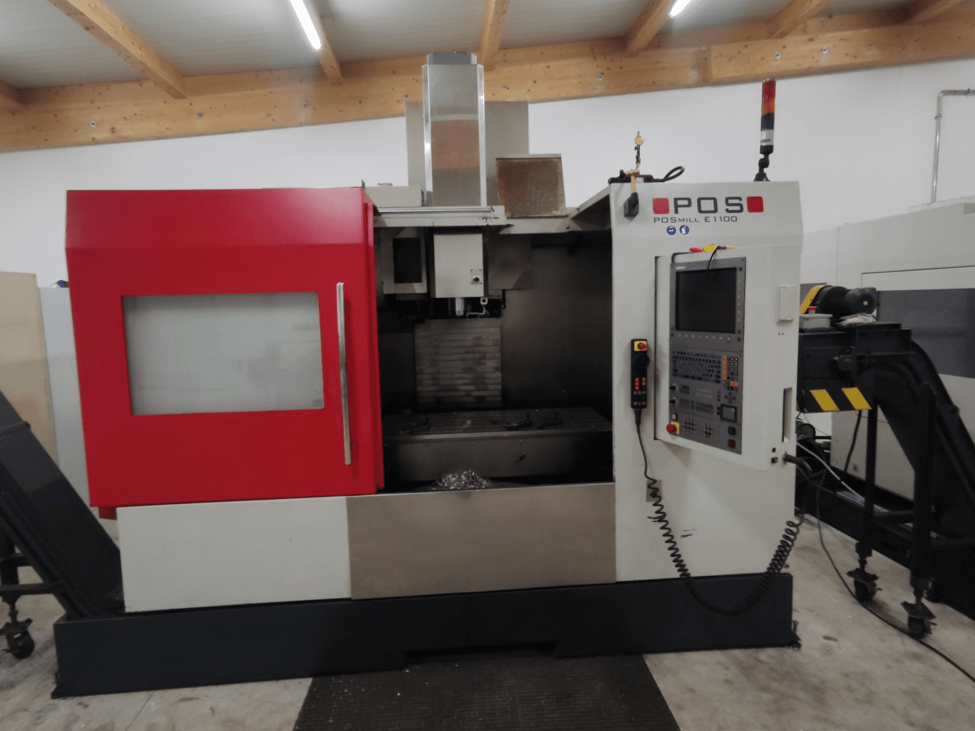 POS PSMILL E1100 CNC frezavimo staklės, vaizdas iš priekio, raudonos ir sidabrinės spalvos korpusas, valdymo skydelis ir saugos kontrolinės lemputės.