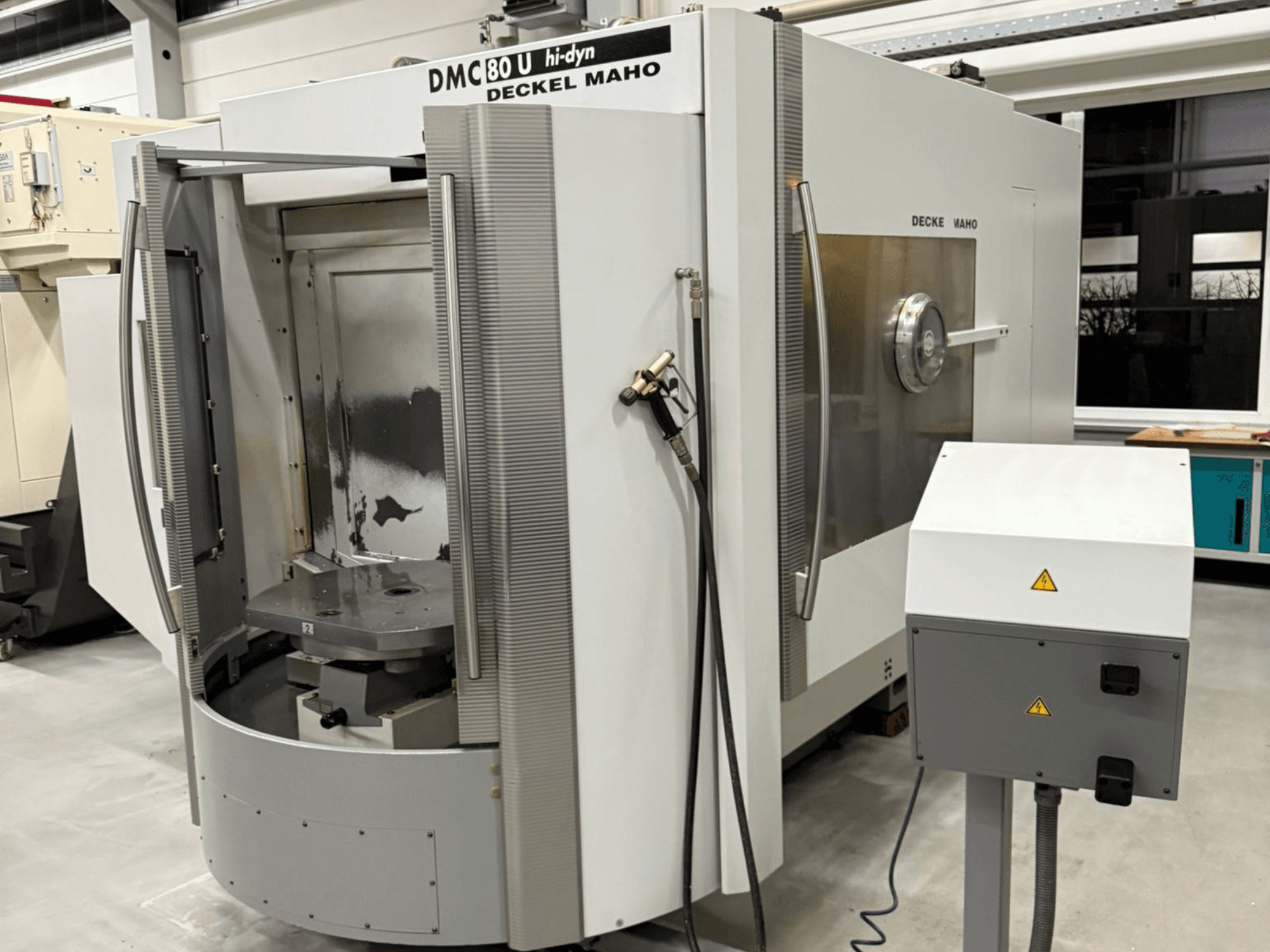 Greitaeigių CNC frezavimo staklių "Deckel Maho DMC 80 U" vaizdas iš priekio, su atviromis įėjimo durelėmis ir valdymo skydeliu šone.