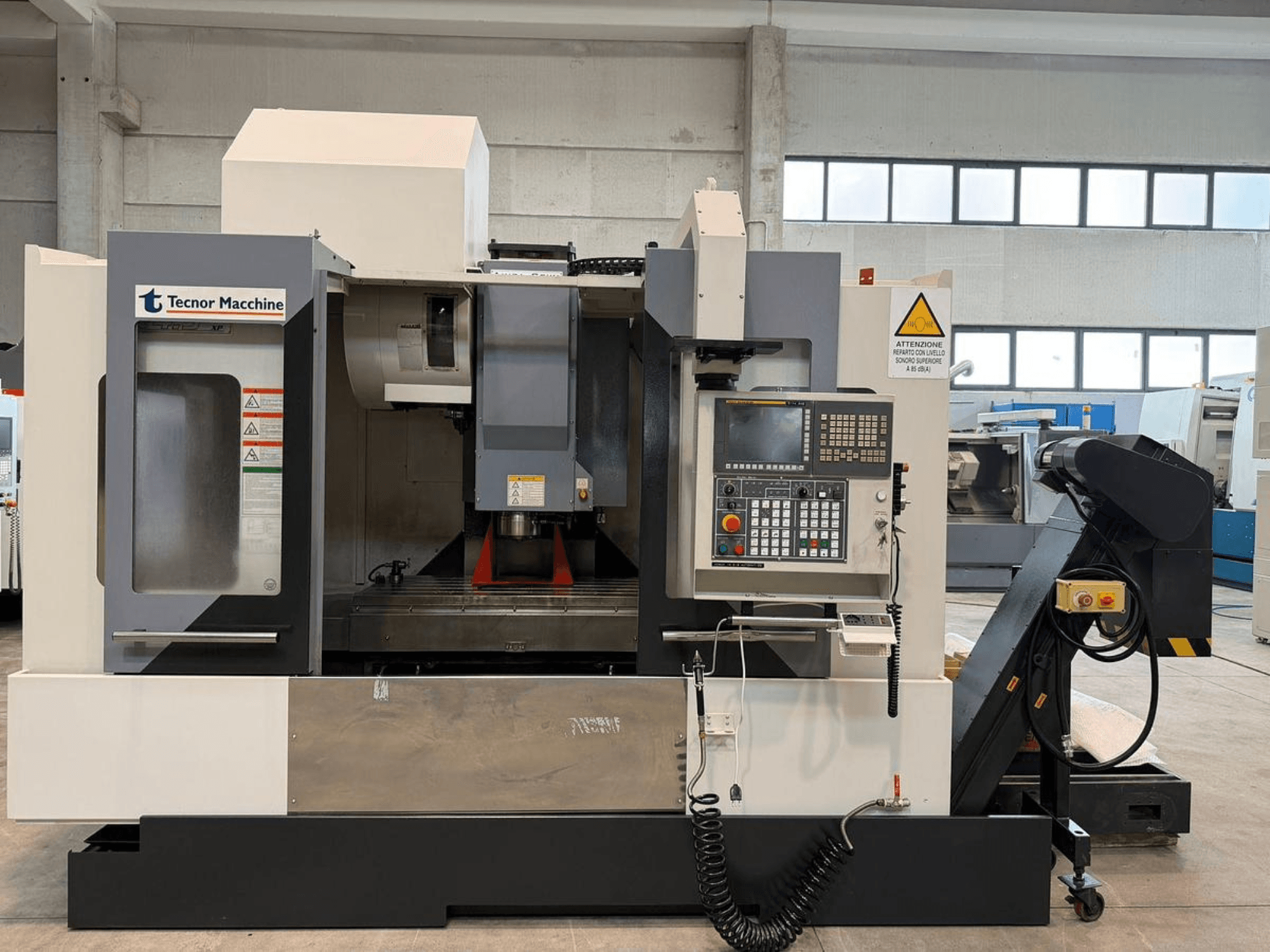 Tecnor Machine CNC frezavimo staklės, vaizdas iš priekio, valdymo skydelis su mygtukais, įspėjamosiomis etiketėmis ir įrankių laikikliu.