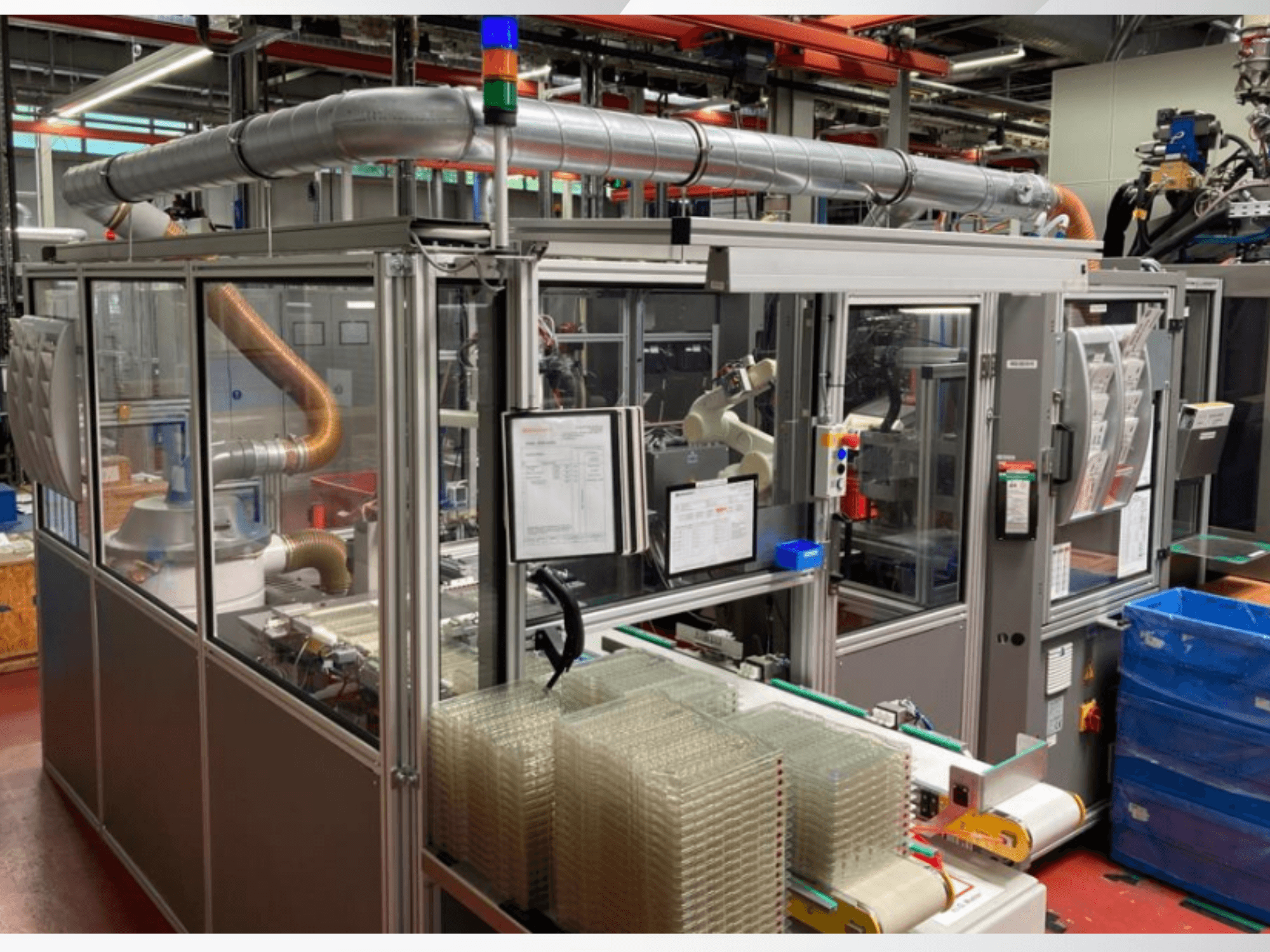 Automatizuotos mašinos su metaliniais vamzdžiais, valdymo pultu ir sukrautomis skaidriomis plastikinėmis talpyklomis gamykloje vaizdas iš priekio.