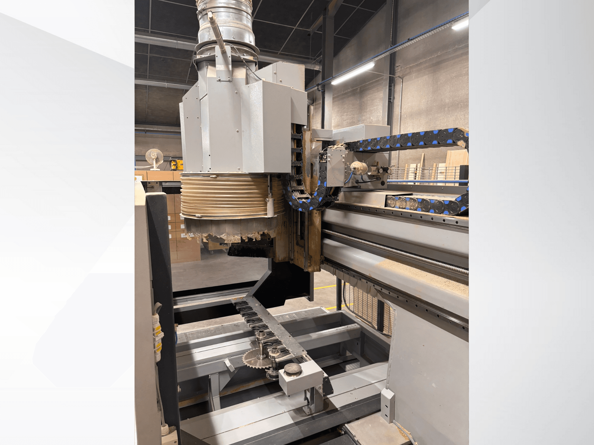 CNC frezavimo staklės su dideliu sukliu ir konvejeriu, vaizdas iš šono, kuriame matomi medienos pjovimo įrankiai ir mašinų komponentai.
