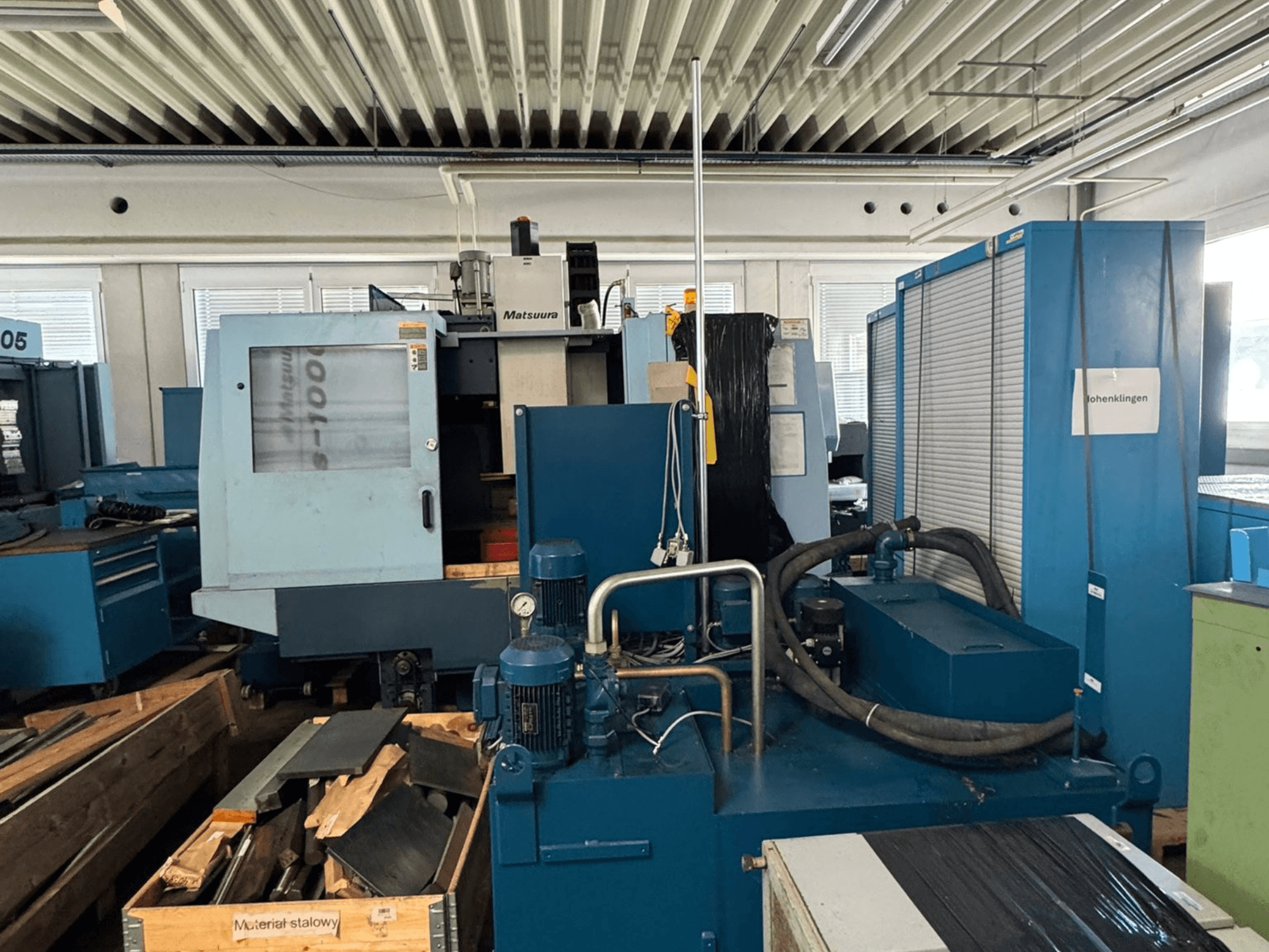 „Matsuura Vplus 1000/40“ vertikaliojo apdirbimo centro vaizdas iš priekio, kuriame matomi valdymo elementai, varikliai ir aplinkinė dirbtuvės aplinka.