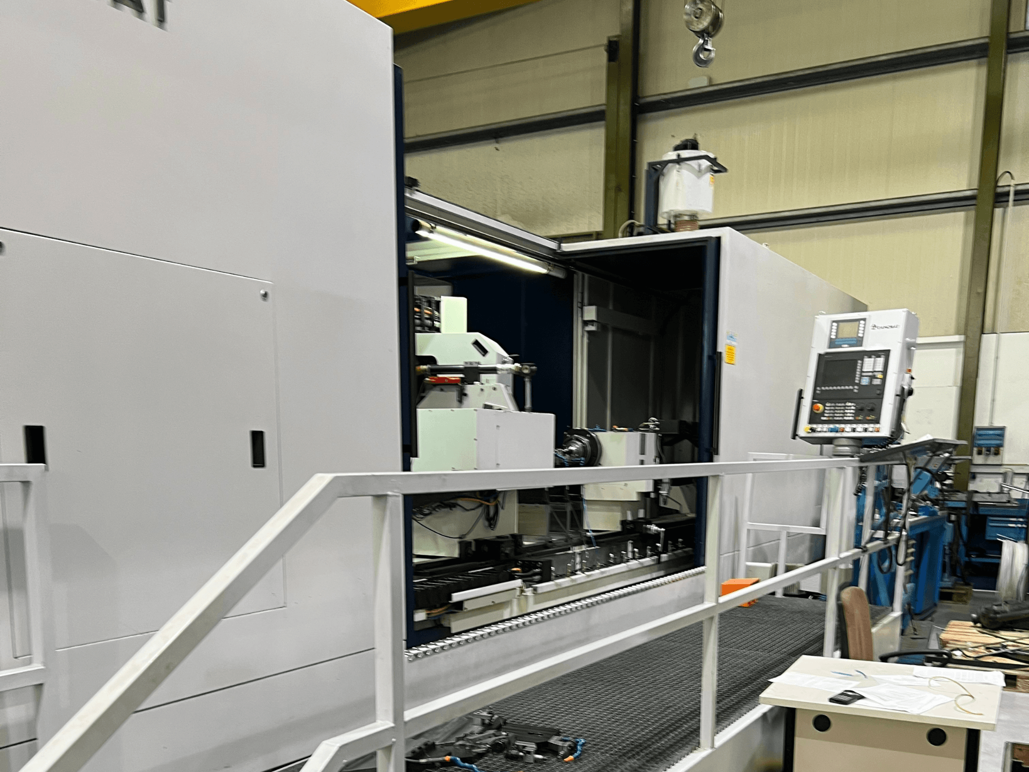 CNC apdirbimo centras su atviru šoniniu vaizdu, kuriame matomi valdikliai, įrankių laikiklis ir pagrindinis viduje esantis komponentas. Prekės ženklo detalių nematyti.