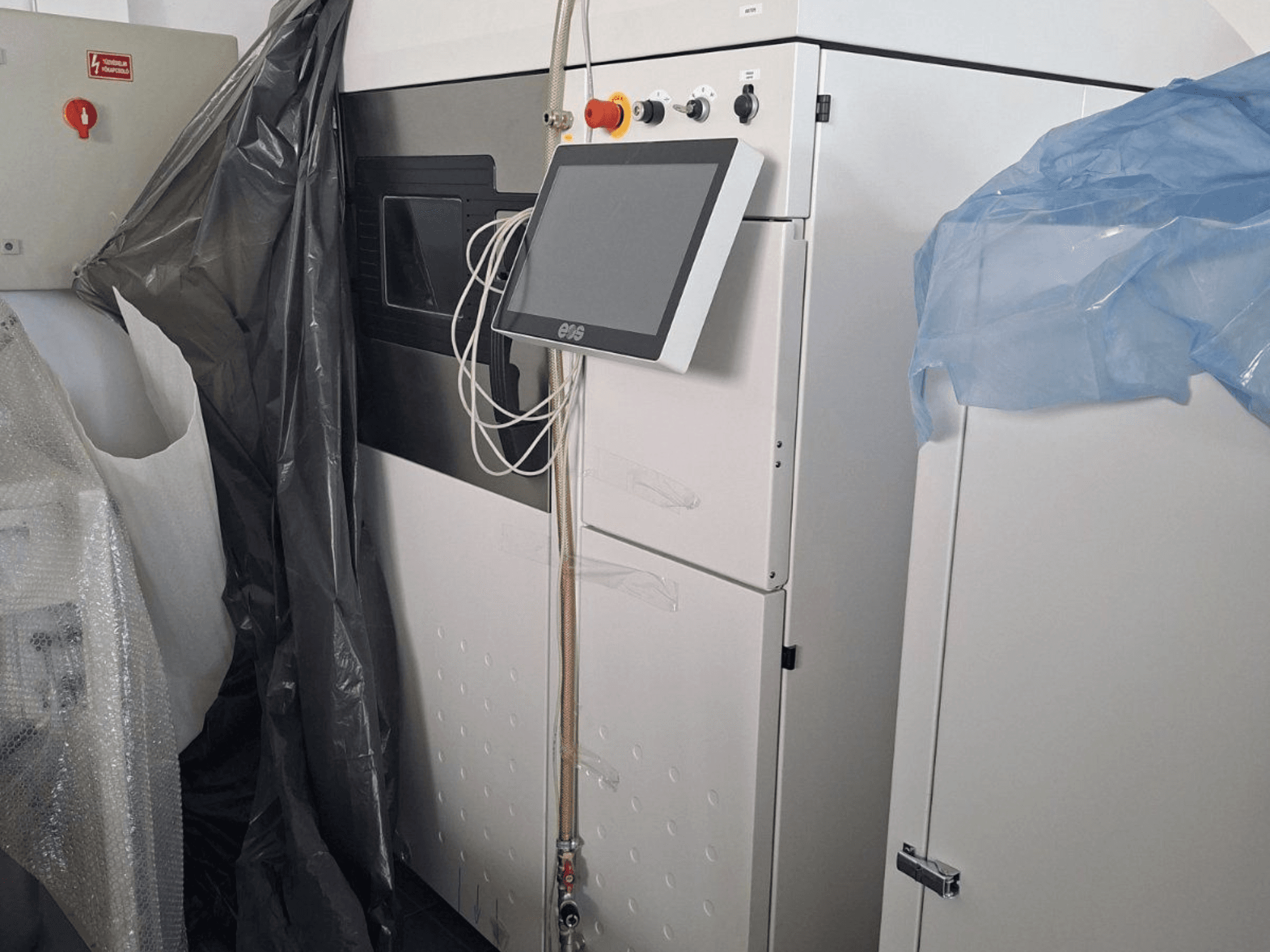 Metalinio 3D spausdintuvo EOS M 290 priekinis vaizdas su jutikliniu ekranu, valdymo skydeliu ir apsauginėmis dangomis.