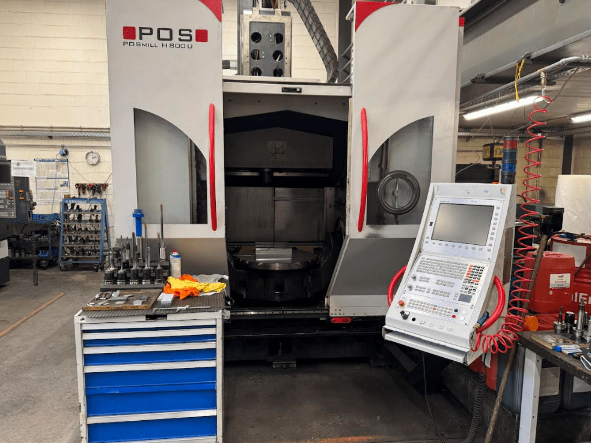 POSMILL H800 U CNC staklės, žiūrint iš priekio, matomas valdymo skydelis ir darbo zona su šalia esančiais įrankiais ir įranga.