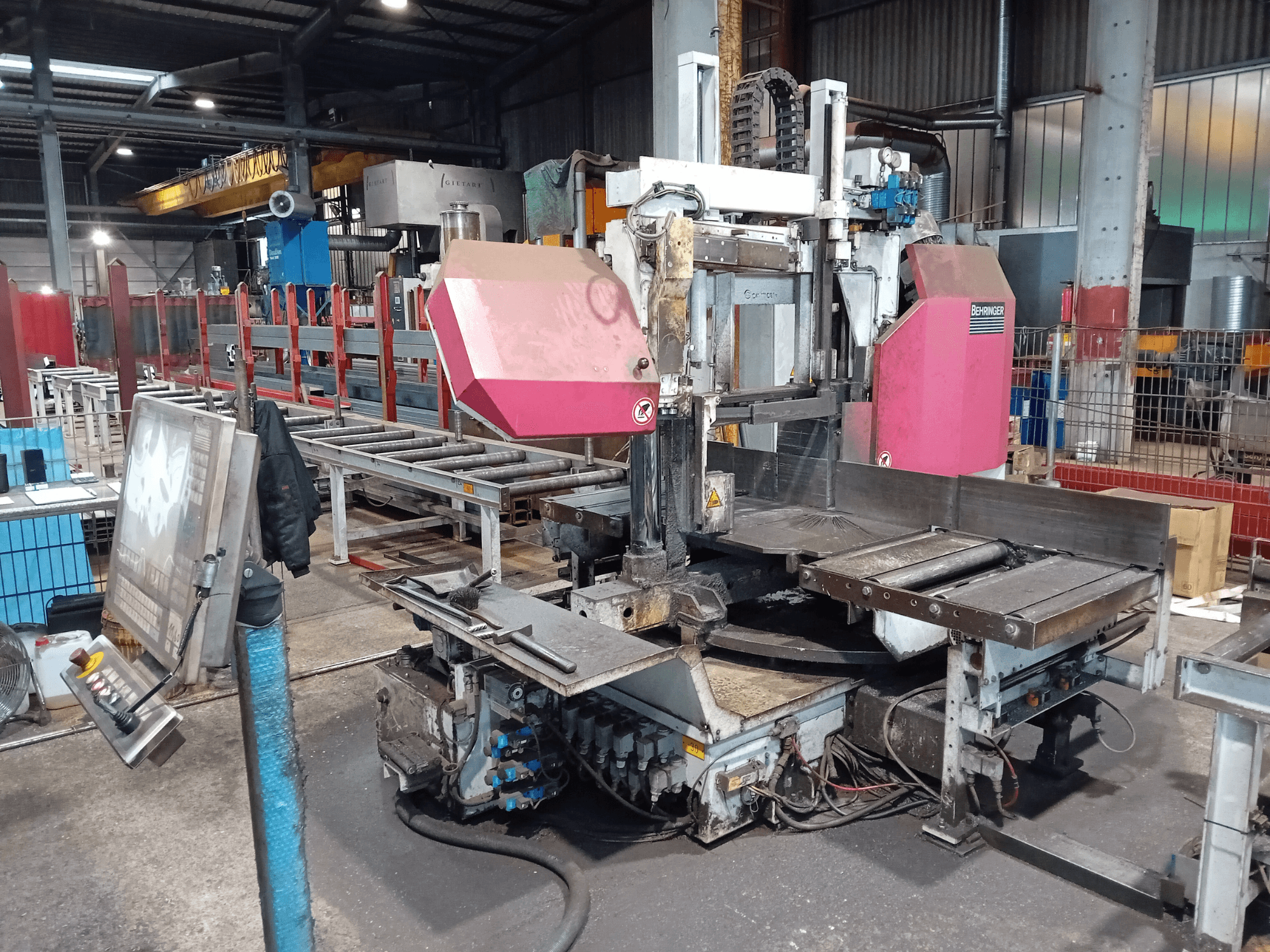 "Behringer" juostinio pjūklo staklės gamykloje, vaizdas iš priekio, didelis pjovimo diskas ir valdymo skydelis su mygtukais.