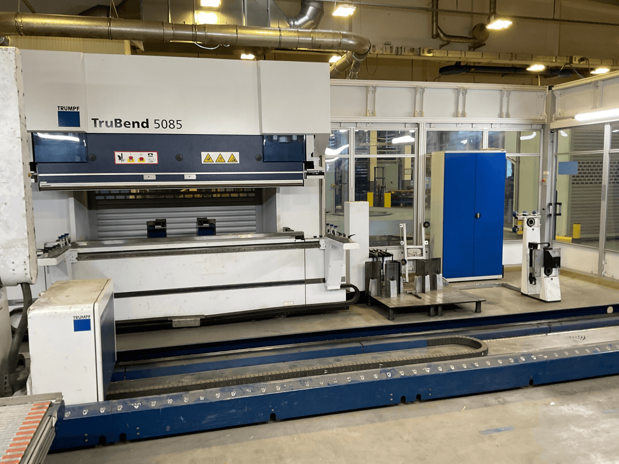 TRUMPF "TruBend 5085", didelių metalo lenkimo staklių vaizdas iš šono su valdymo skydeliu ir įvairiais įrankiais šalia jo.