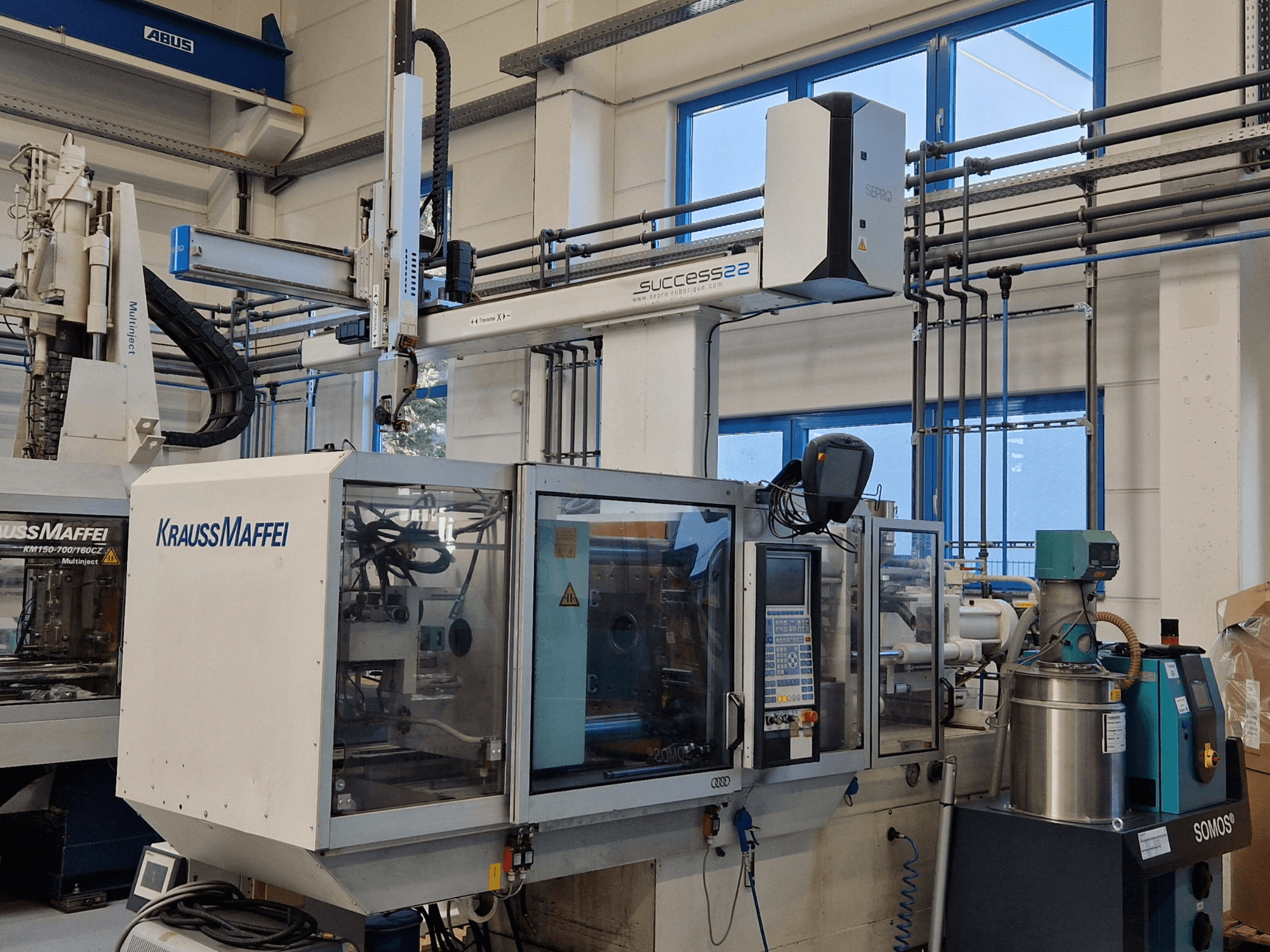 "KraussMaffei Success 22" įpurškimo liejimo mašina su valdymo skydeliu, žiūrint iš priekio gamykloje.