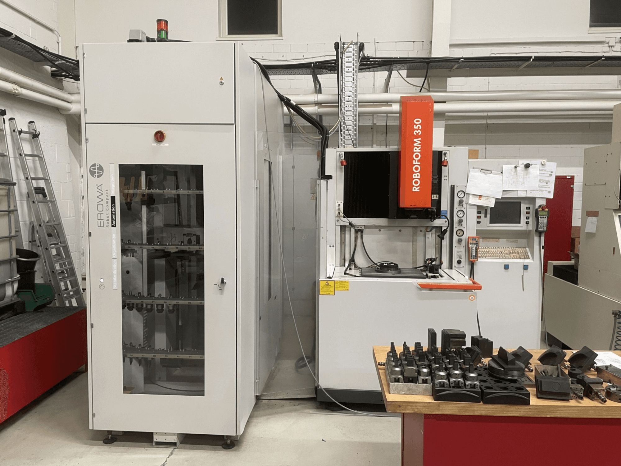 Presavimo staklės CHARMILLES Roboform 350, vaizdas iš priekio, su įrankiais, išdėstytais ant stalo, ir greta esančia įranga.