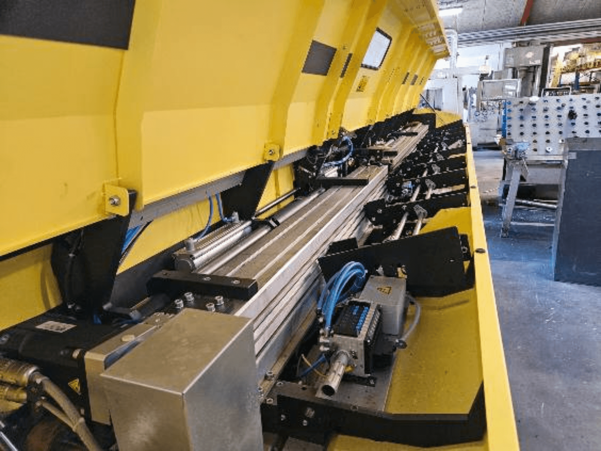 Geltonos hidraulinės mašinos su metaliniais komponentais ir konvejerio bėgiais, su žarnomis ir elektroninėmis dalimis, vaizdas iš arti.