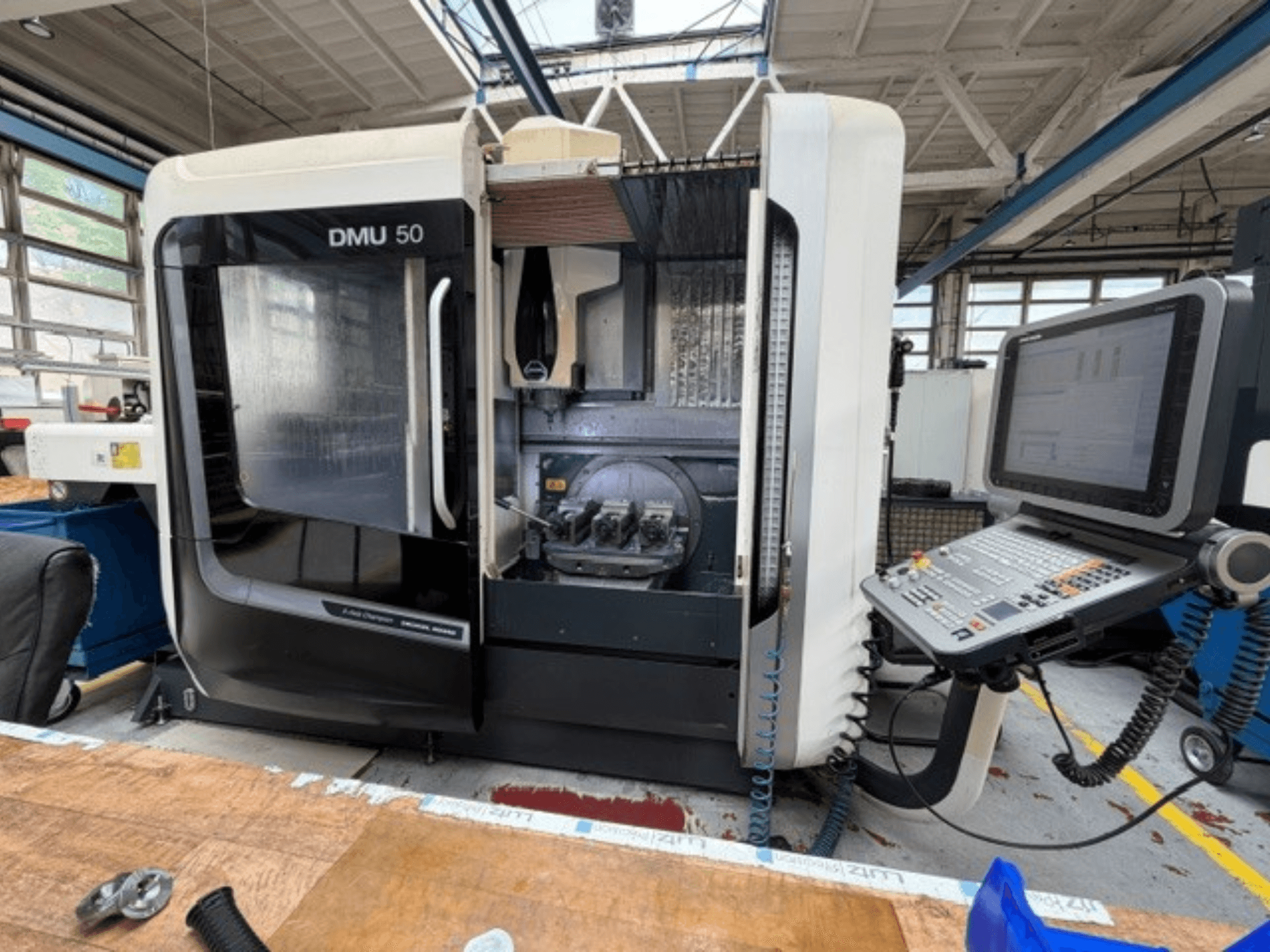 DMG MORI DMU 50 trečiosios kartos vertikalusis apdirbimo centras, vaizduojamas iš priekio: atidarytos durys, matomas CNC valdymo pultas ir darbo erdvė viduje.