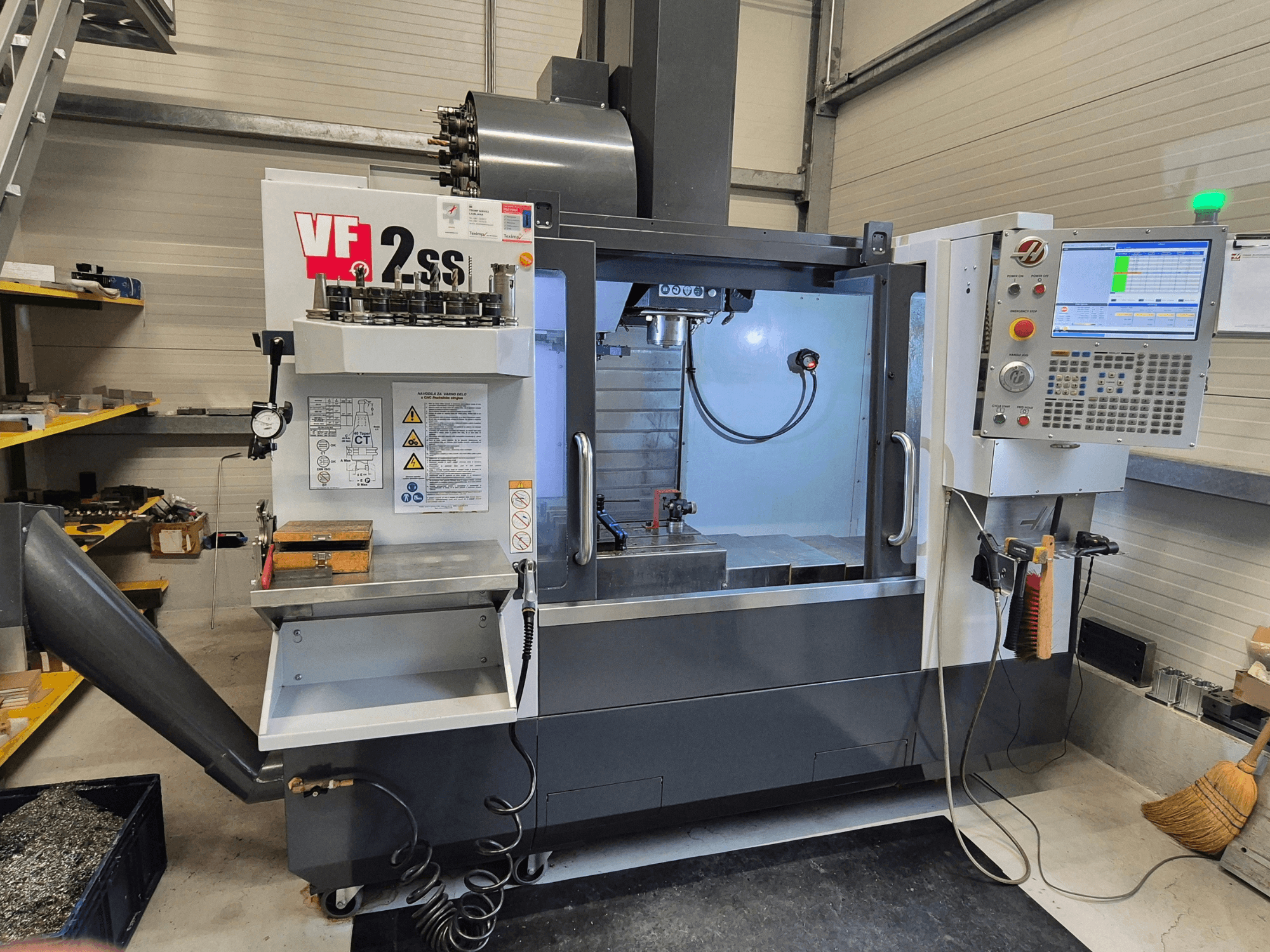HAAS VF2 SS-EU vertikalusis apdirbimo centras iš priekio, kuriame matomi valdikliai, suklys ir apdirbimo zona.