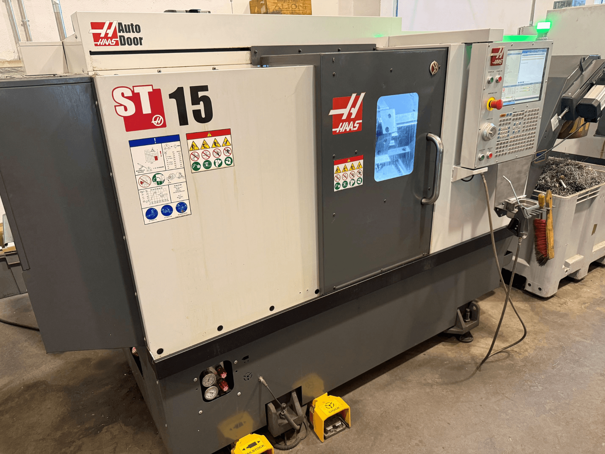 HAAS ST 15 horizontalus tekinimo staklės, vaizdas iš priekio, kuriame matomas valdymo pultas, automatinės durys ir techniniai rodikliai.
