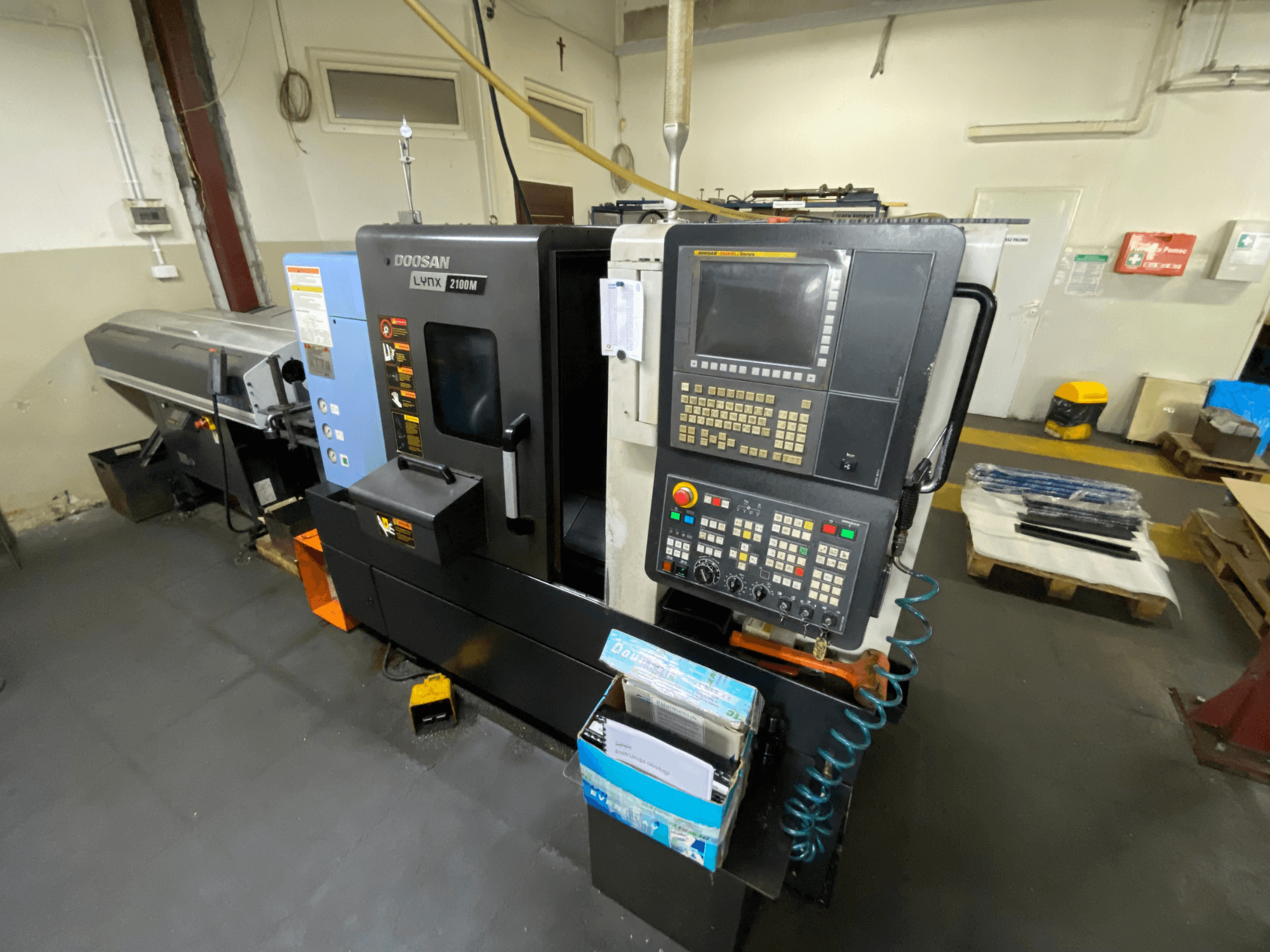 „DOOSAN LYNX 2100MA“ horizontalios tekinimo staklės, matomos iš šono, su valdymo pultu, įrankiais ir darbo zona.