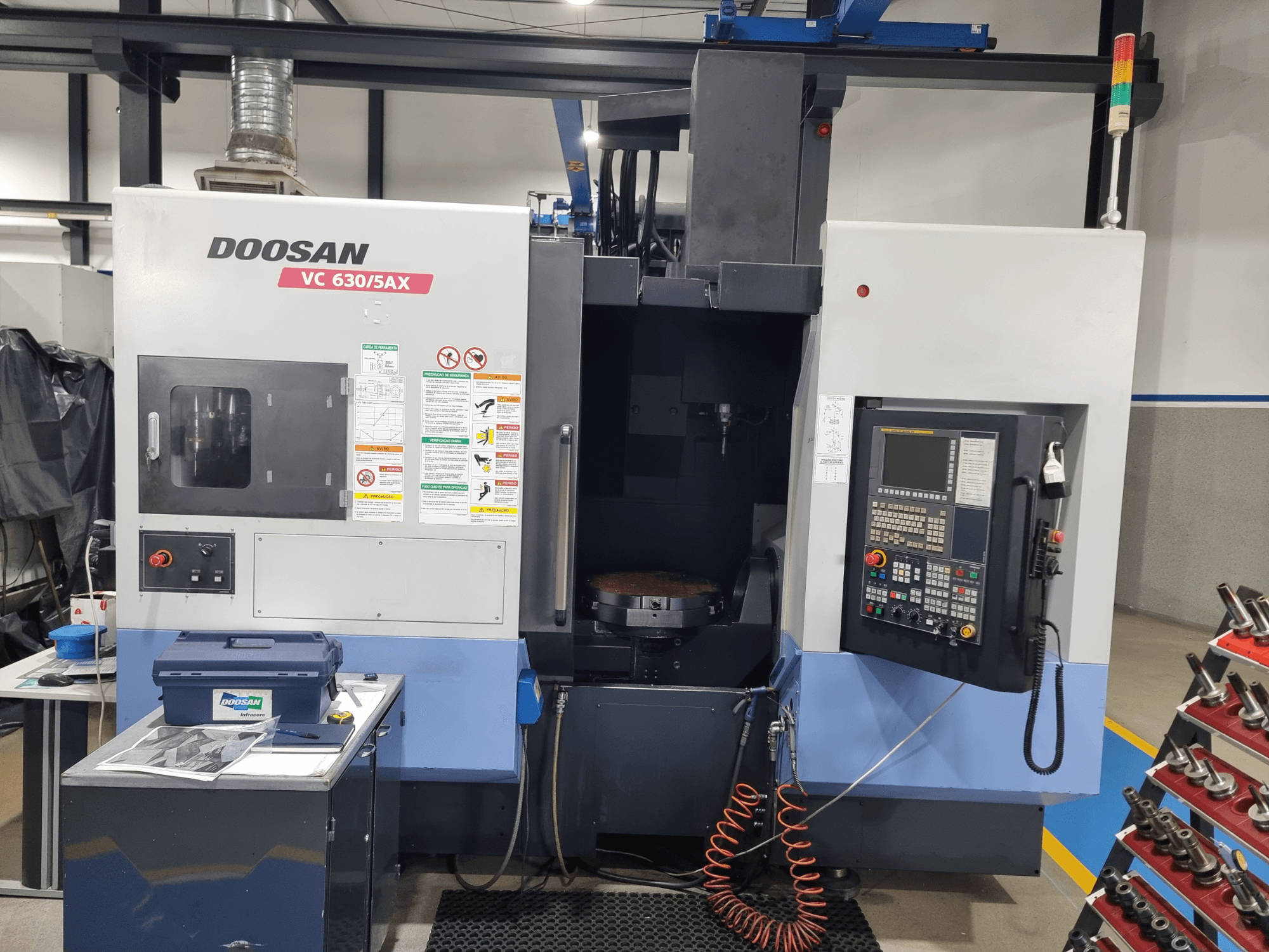 Universalus apdirbimo centras „DOOSAN VC 630/5AX“, vaizdas iš priekio, kuriame matomas valdymo skydas, apdirbimo zona ir saugos įranga.