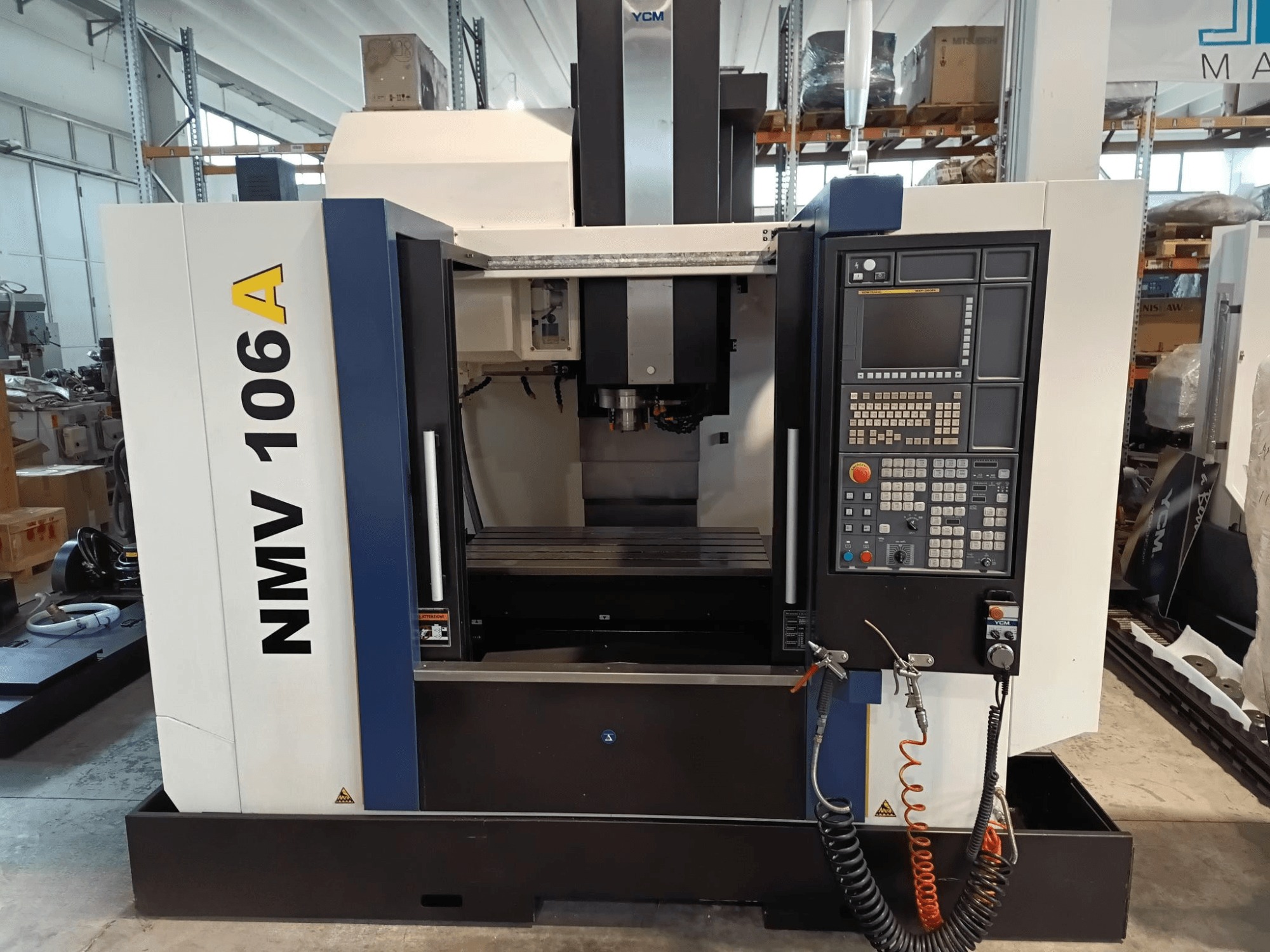 YCM NMV 106A apdirbimo centras, vaizdas iš priekio, valdymo skydelis su mygtukais ir aušinimo skysčio žarnomis.