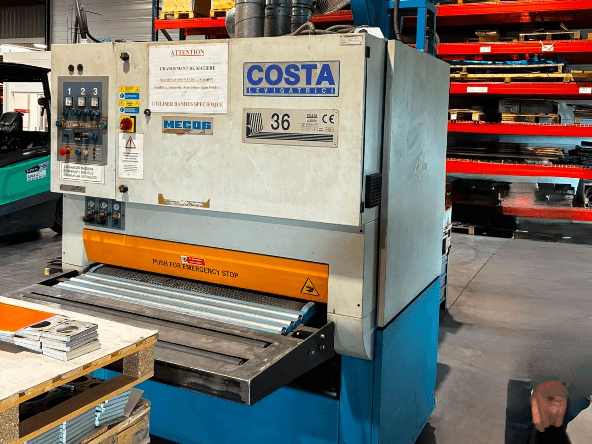 „Costa M36 CCS 1150“ nušlifavimo staklių šoninis vaizdas, kuriame matomas valdymo pultas, avarinio sustabdymo mygtukas ir konvejerio paviršius.