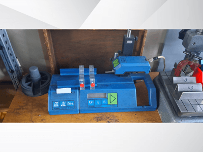 "Hommel" spausdintuvo P 1010 ir testerio T1000 šoninis vaizdas, mėlynas korpusas, mygtukai ir raudoni indikatoriai ant darbo stalo.