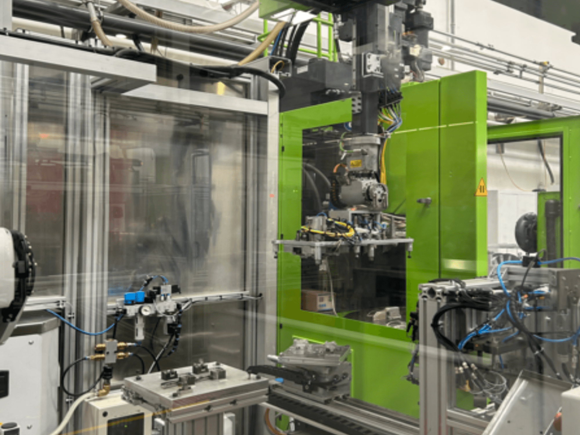 Pramoninės robotų mašinos žaliame korpuse, kuriame matomi mechaniniai komponentai ir vamzdynai, žiūrint iš priekio.