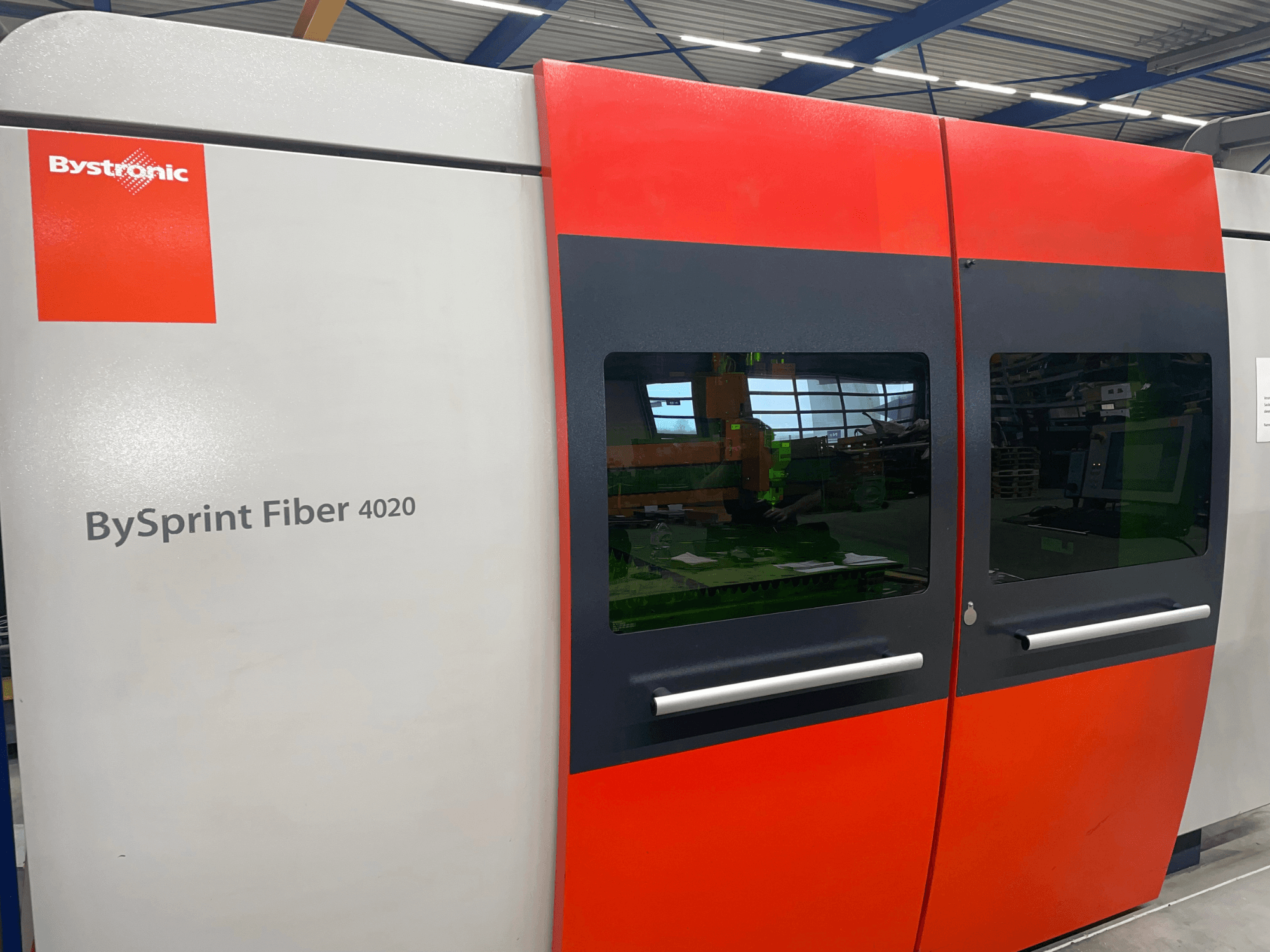 "Bystronic BySprint Fiber 4020" priekinis vaizdas, pilkos ir raudonos spalvos skydelis su dideliais langais ir viduje matoma valdymo sąsaja.