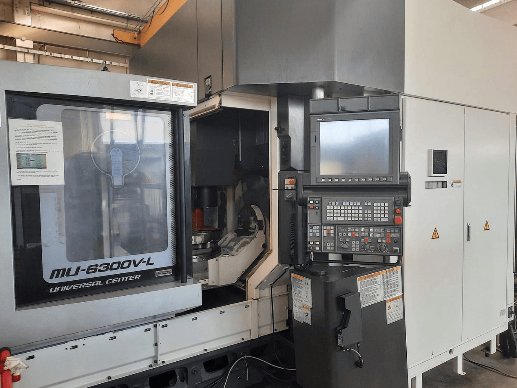 Universalaus centro MU-6300V-L staklės, parodytos iš priekio, matomas valdymo skydelis, ekranas ir naudojimo instrukcijos.