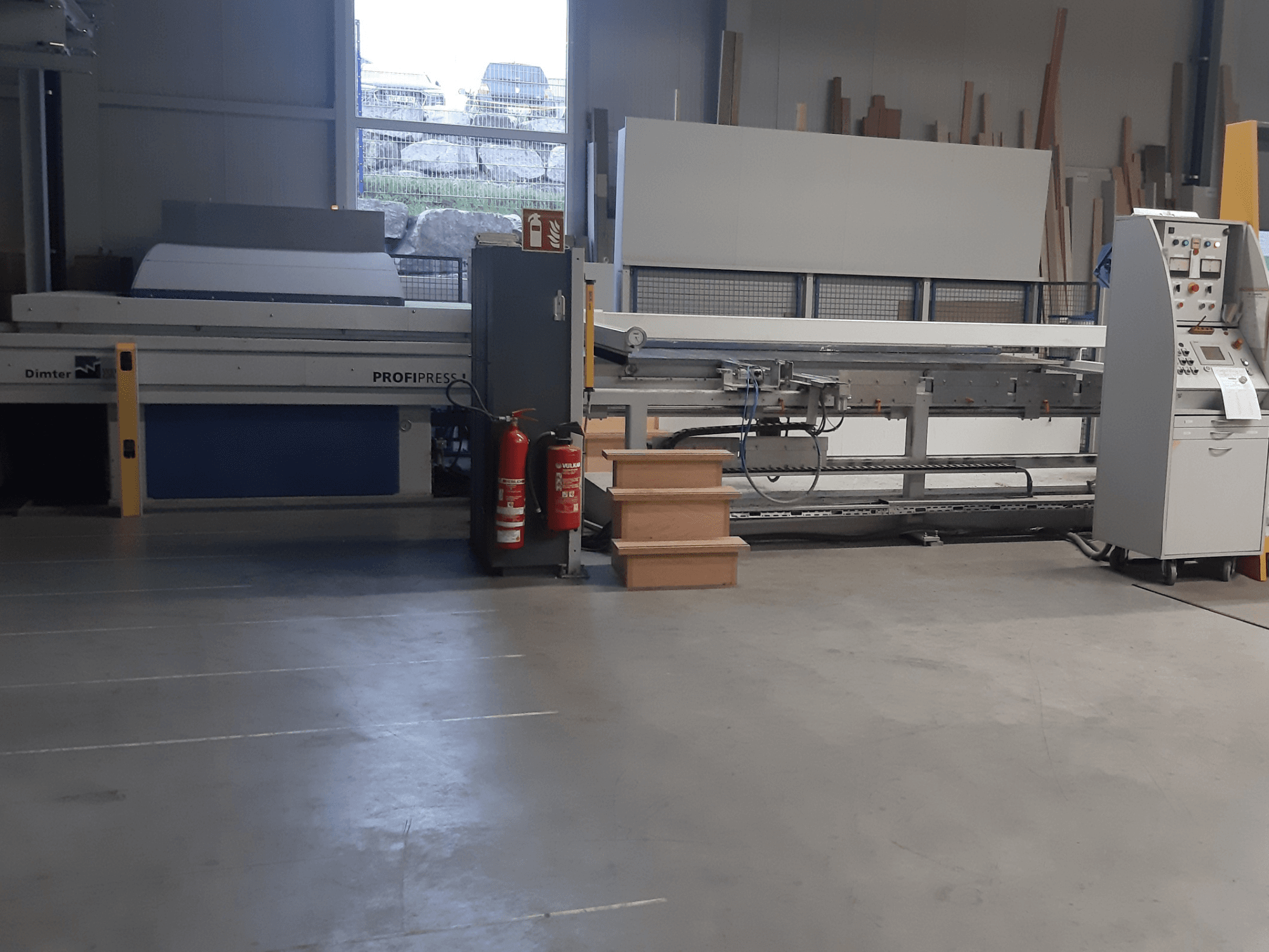 Dimter ProfiPress mašina dirbtuvėse, žiūrint iš priekio, su valdymo pultu ir gesintuvais šalia.