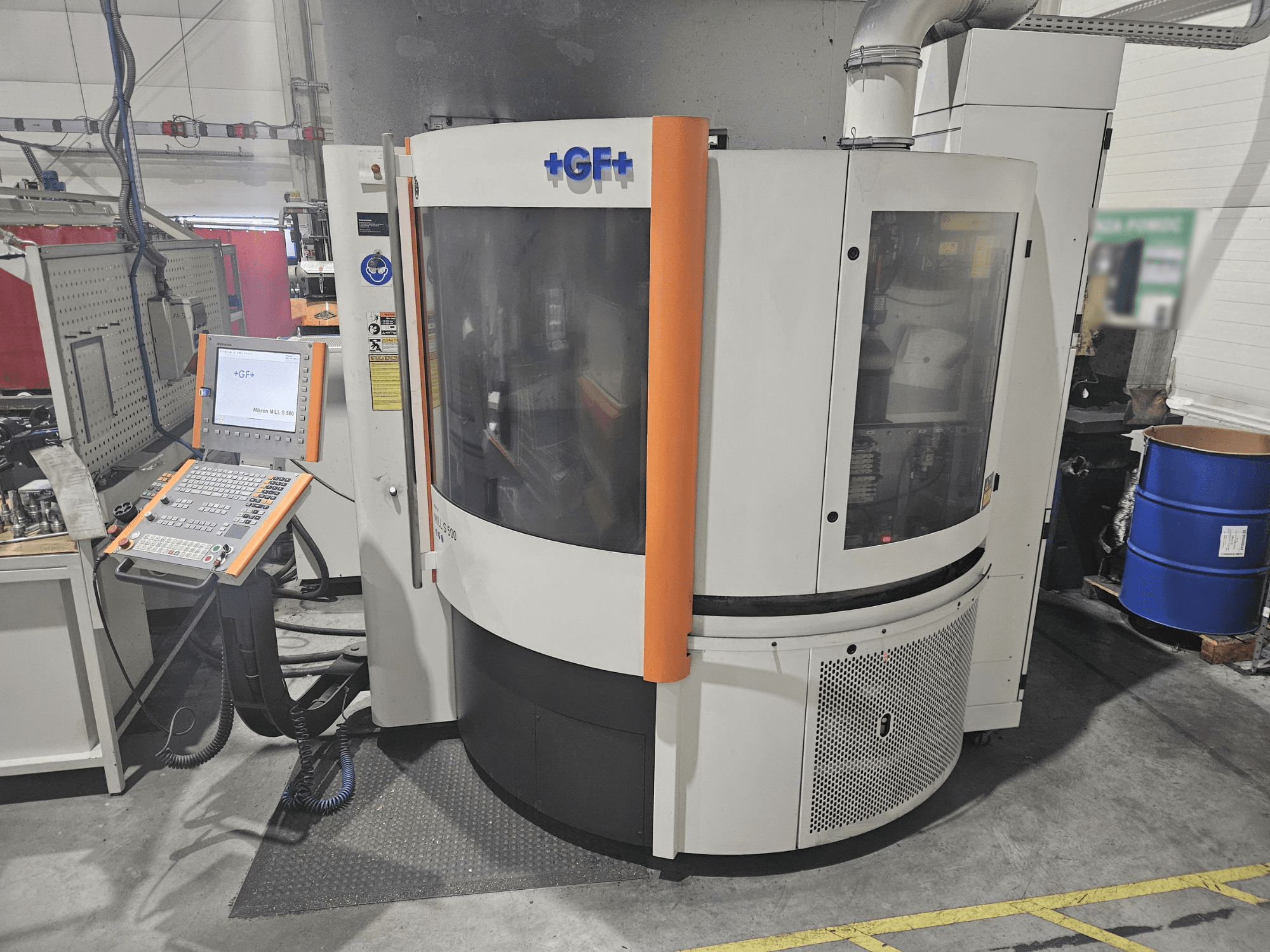 "GF Machining Solutions" staklės su valdymo skydeliu, vaizdas iš priekio; permatomas skydelis, oranžiniai akcentai ir pramoninis nustatymas.