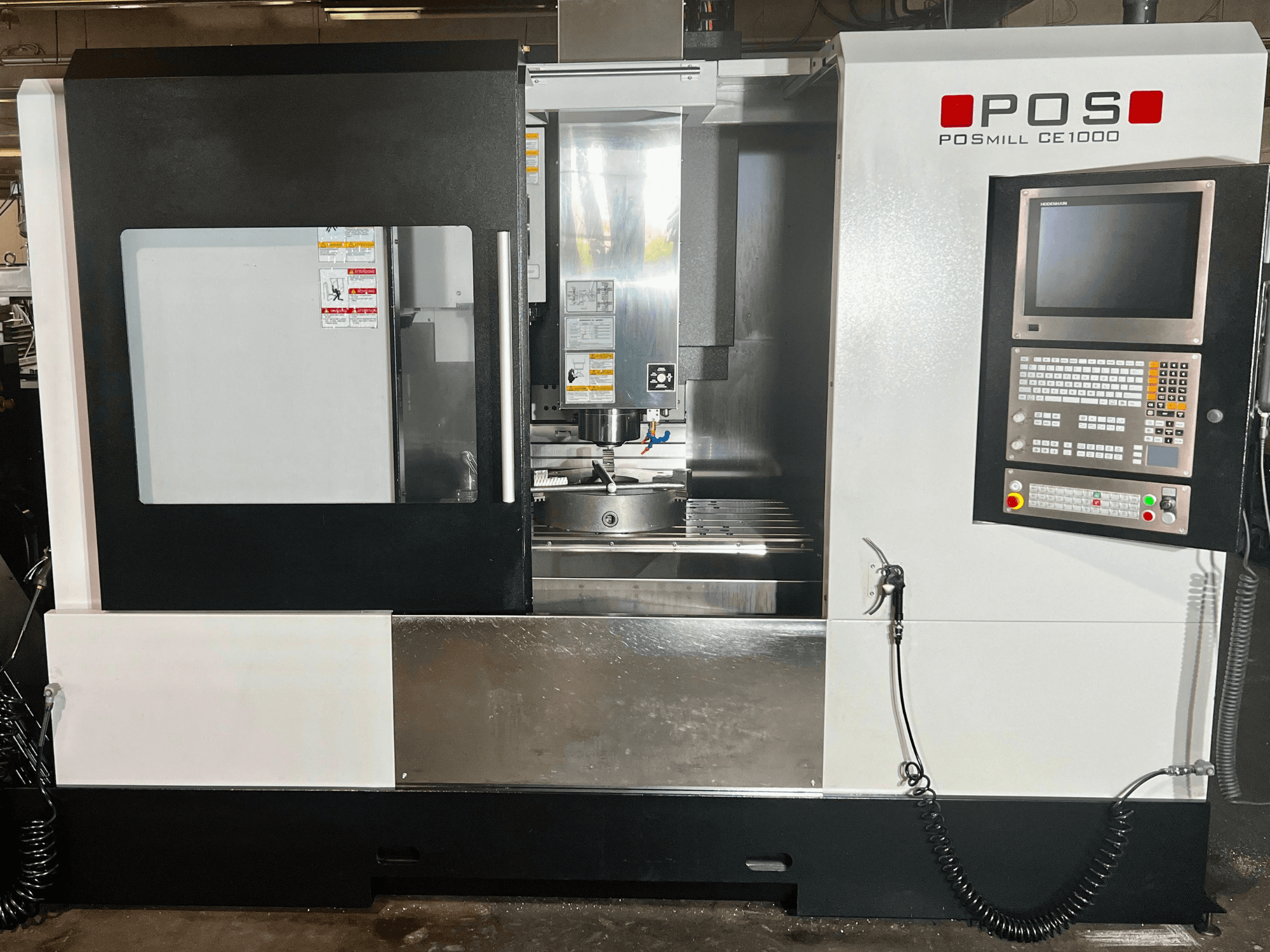 Vertikaliojo apdirbimo centro „POSmill CE1000“ vaizdas iš priekio, kuriame matomas valdymo pultas, langas ir metaliniai paviršiai.