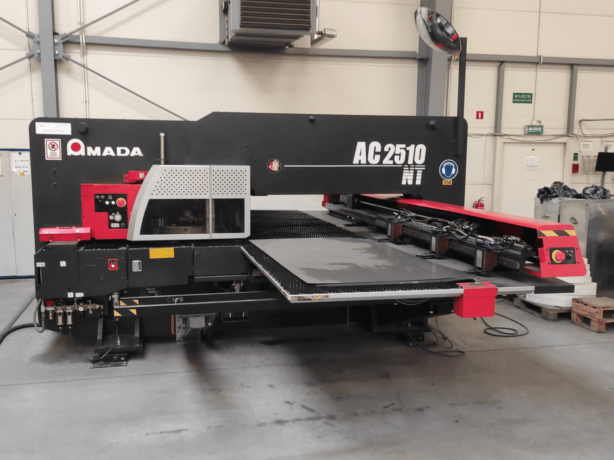 "Amada AC2510 NT" CNC štampavimo staklės, vaizdas iš priekio, su valdymo skydeliu ir lakštų pakrovimo zona.