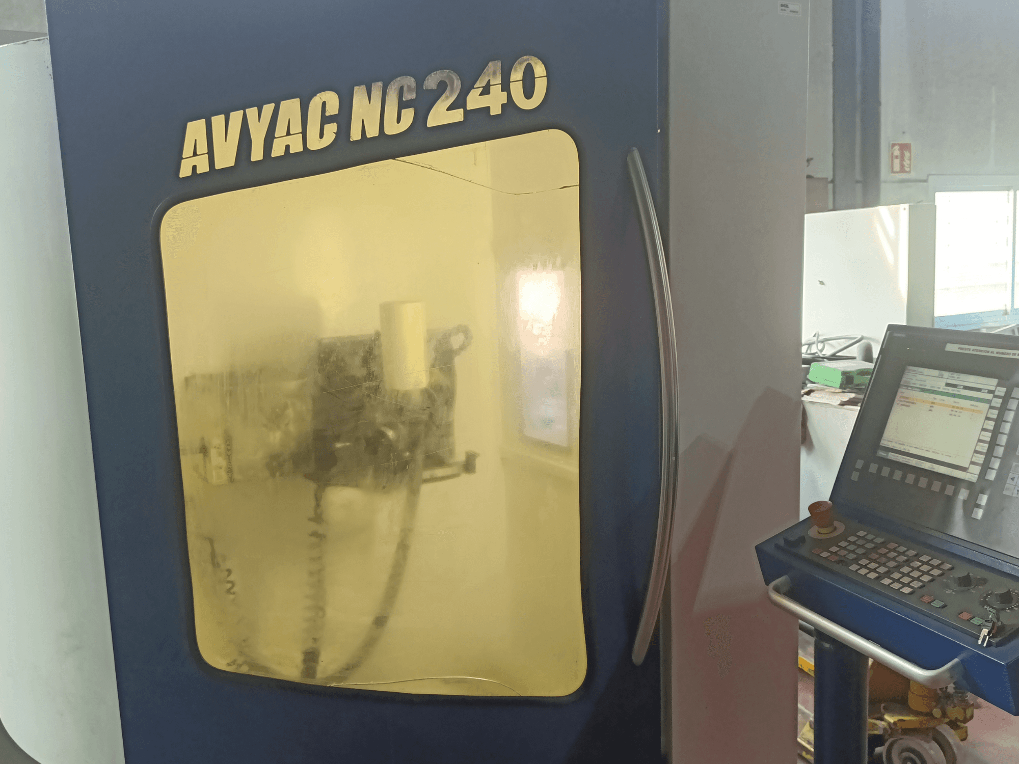 AVYAC NC240 cilindrinio šlifavimo staklės, šoninis vaizdas, kuriame matomas valdymo skydelis ir iš dalies pro langą matoma šlifavimo zona.