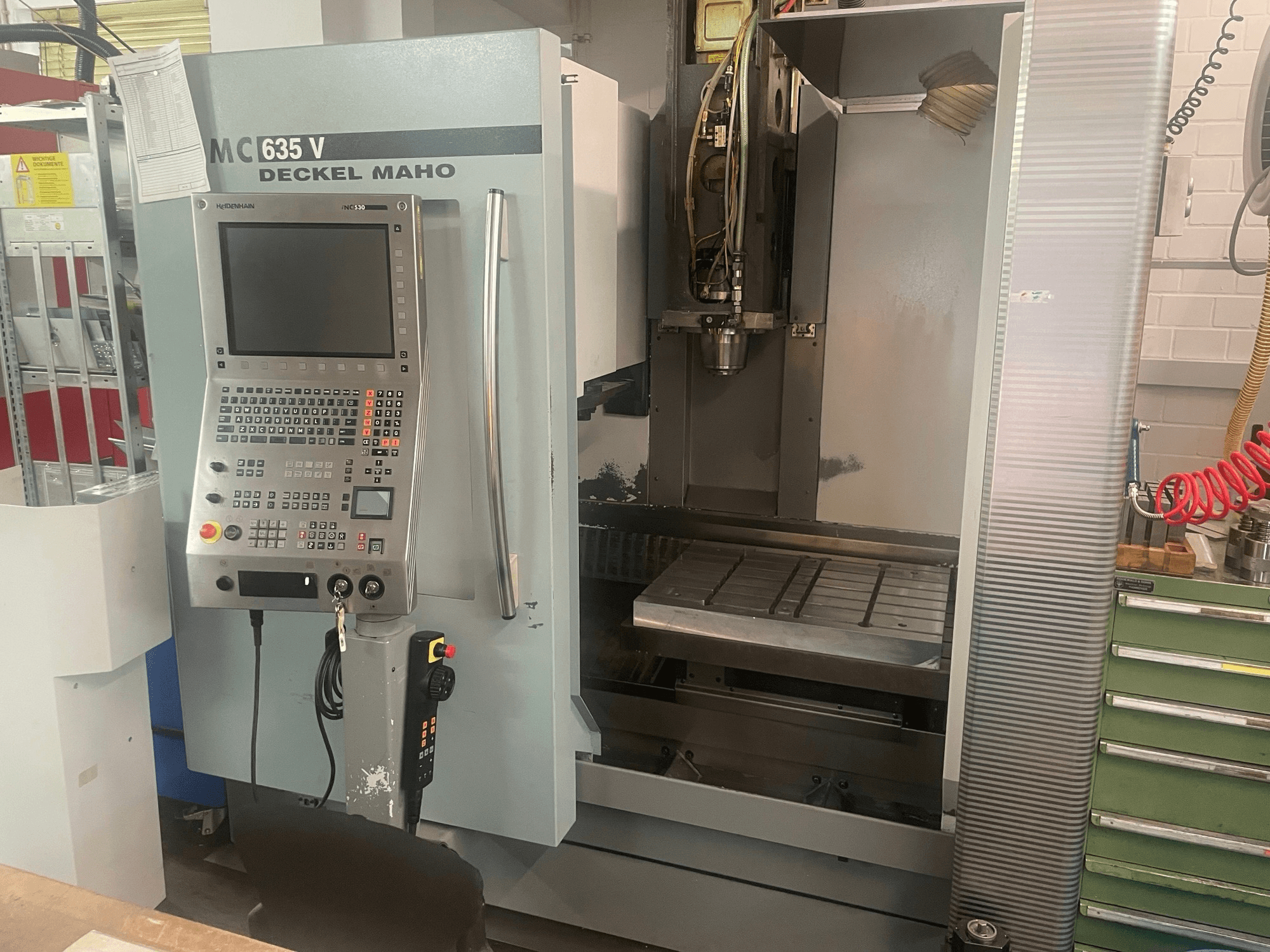 Vertikalaus apdirbimo centro „DECKEL MAHO DMC 635 V“ vaizdas iš priekio su valdymo pultu ir atvira darbo zona, kuriame matoma įrankio galvutė ir staklės pagrindas.