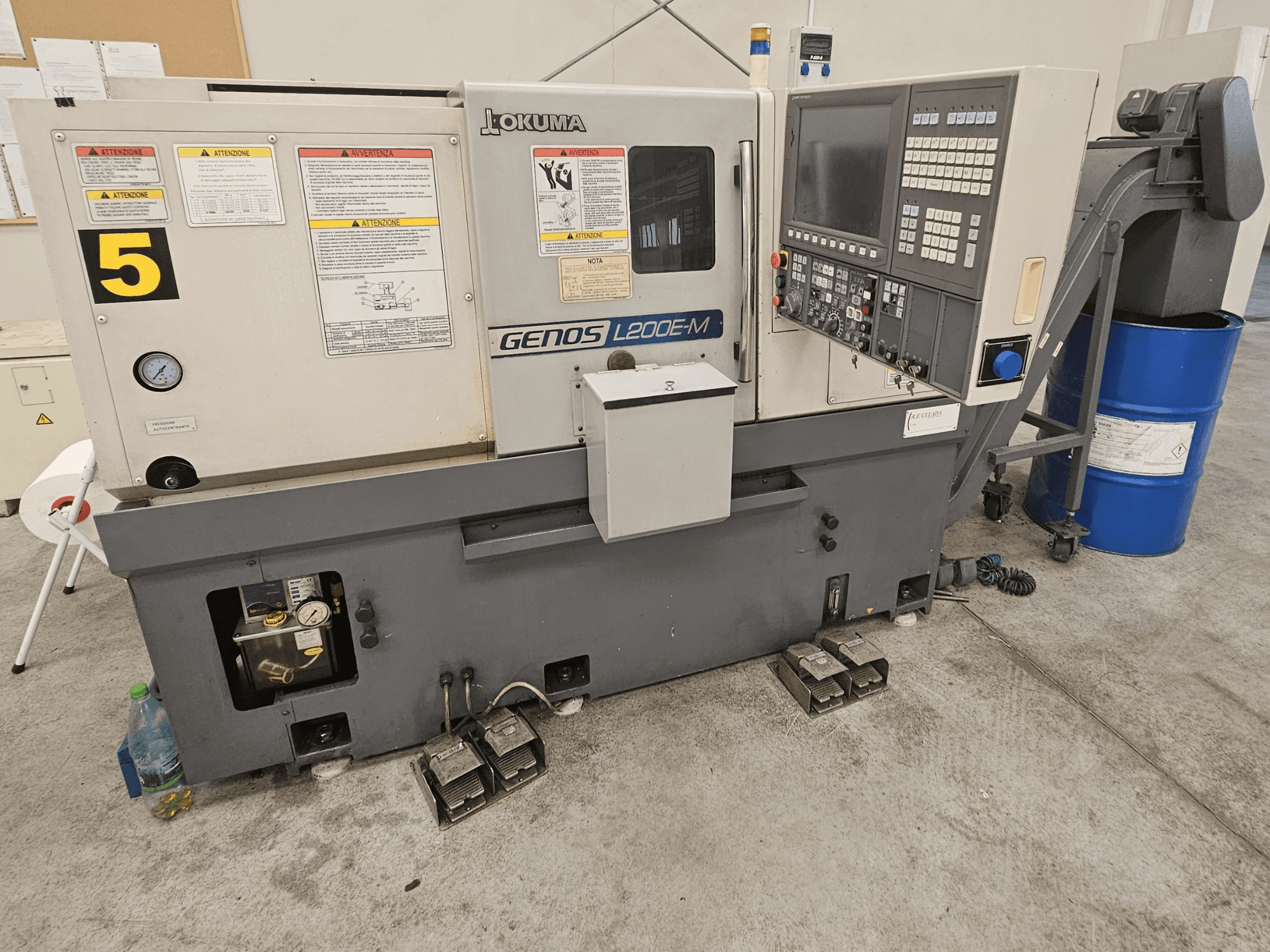 Okuma GENOS L200E-M horizontaliosios tekinimo staklės iš priekio, su valdymo skydeliu, etiketėmis ir aušinimo skysčio statine.