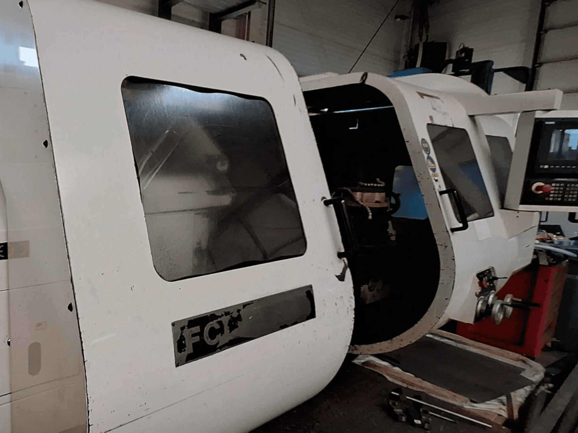 Baltos CNC staklės su matomu valdymo skydeliu ir atidarytomis durelėmis, kuriose matyti vidiniai komponentai; vaizdas iš priekio. Prekės ženklas: FCT.