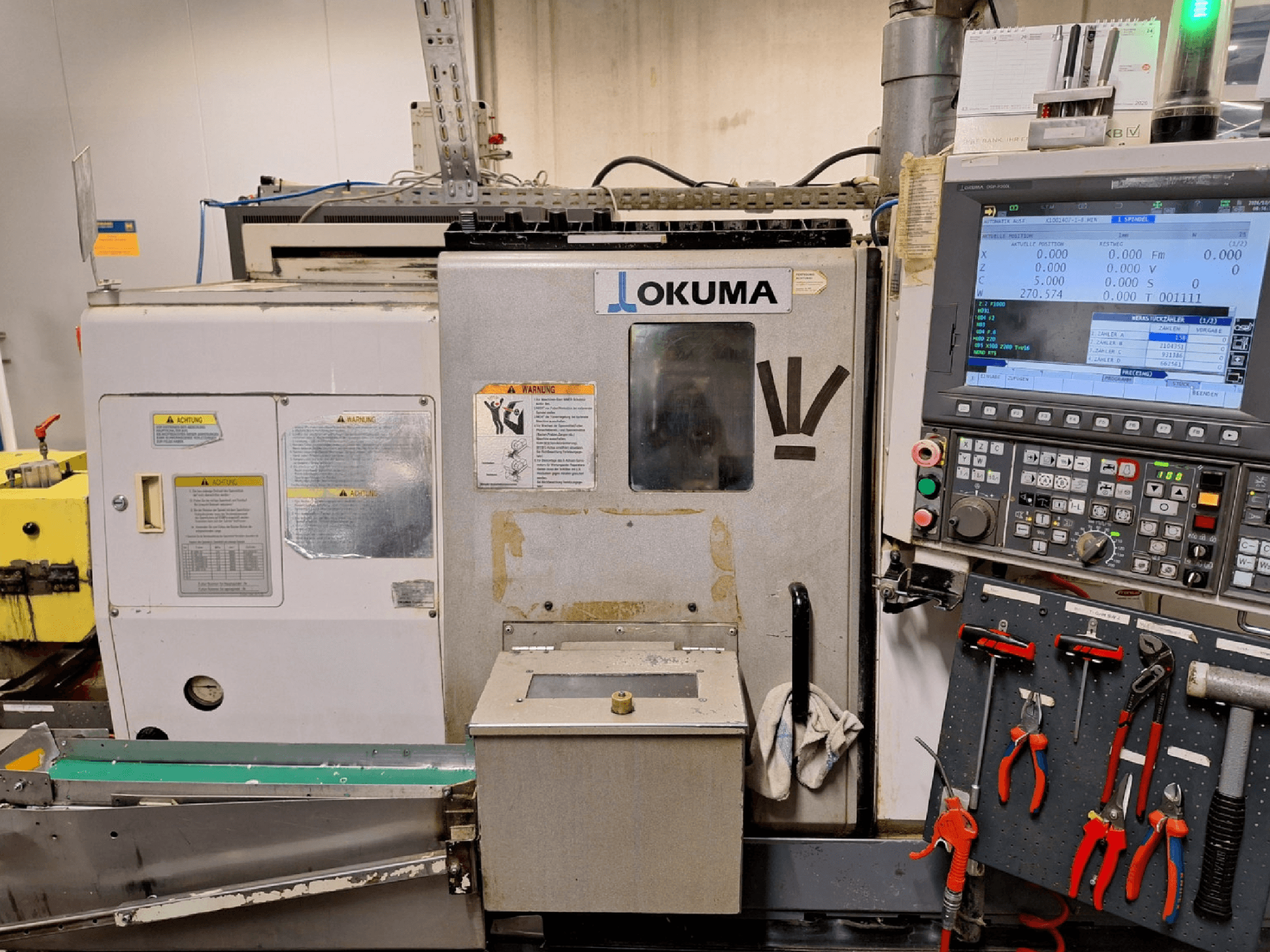 „Okuma LB200-MW“ horizontalus tekinimo staklės, vaizdas iš priekio, šone matomas valdymo pultas ir įrankiai.