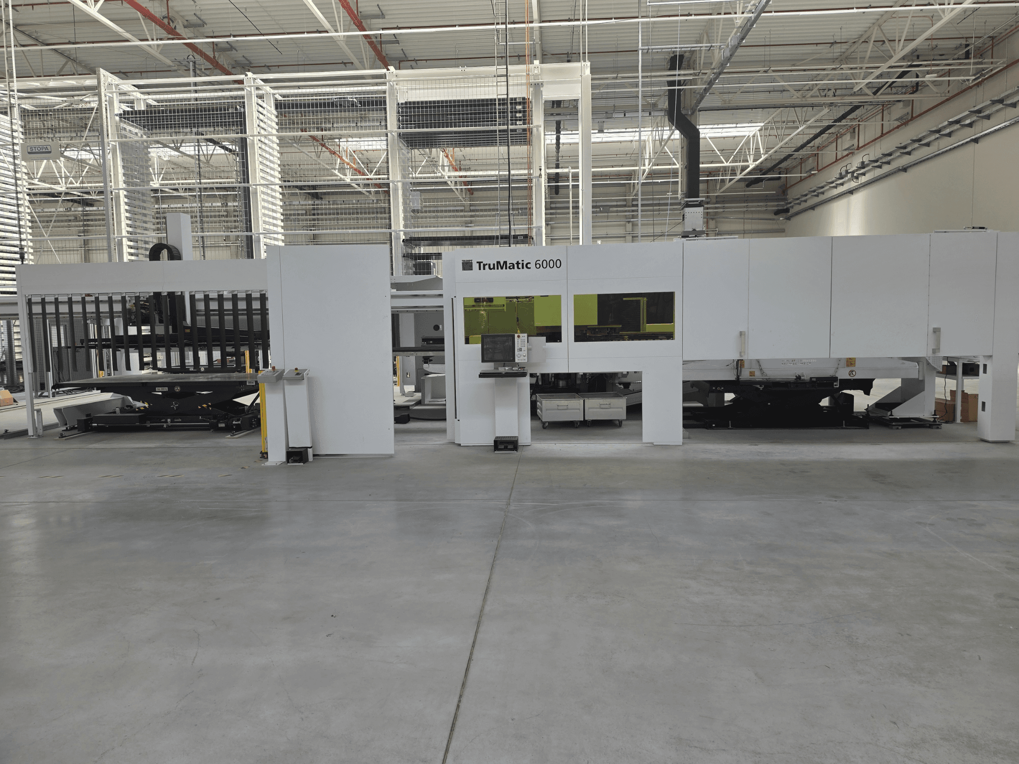 „TRUMPF TruMatic 6000“ automatizuota lakštinio metalo gamybos sistema, vaizdas iš priekio, kuriame matomas valdymo pultas ir pakrovimo zona.