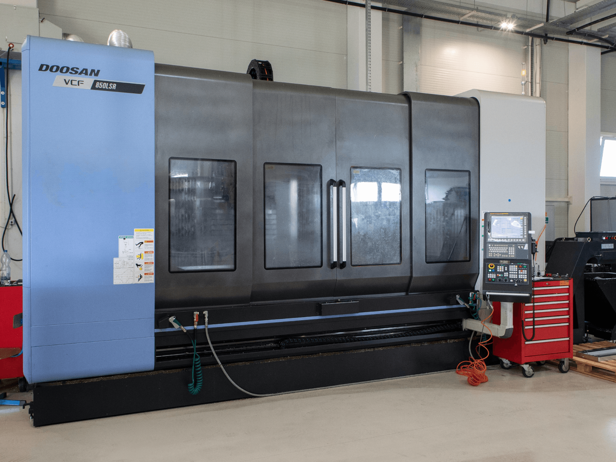„DOOSAN VCF850“ frezavimo ir tekinimo centras, vaizdas iš priekio; jame įrengti dideli dvigubi langai, valdymo pultas ir įrankių laikymo vieta. Idealiai tinka apdirbimui.