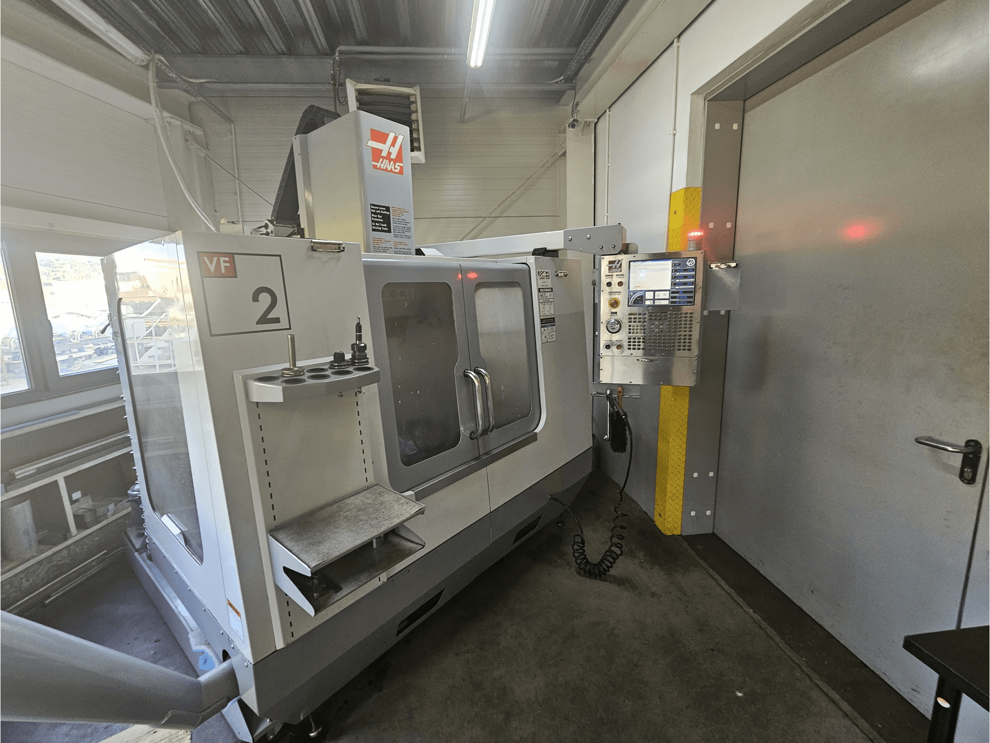 Haas VF-2 CNC frezavimo staklės, vaizdas iš priekio, kuriame matomas valdymo skydelis, įrankių laikikliai ir skaidrus darbo vietos langas.