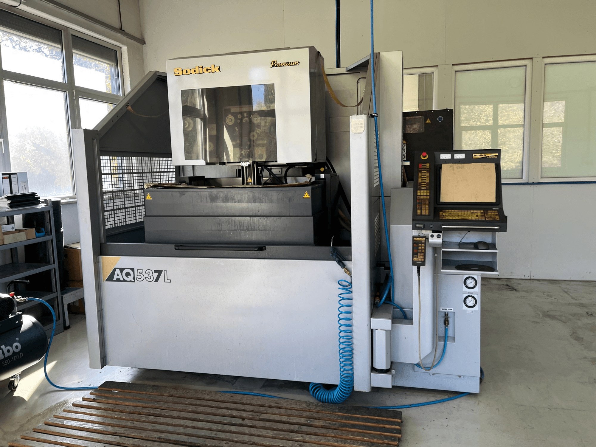 Sodick AQ537L elektros išlydžio staklių (EDM) priekinis vaizdas su valdymo skydeliu, vandens aušinimo linijomis ir darbo vieta.