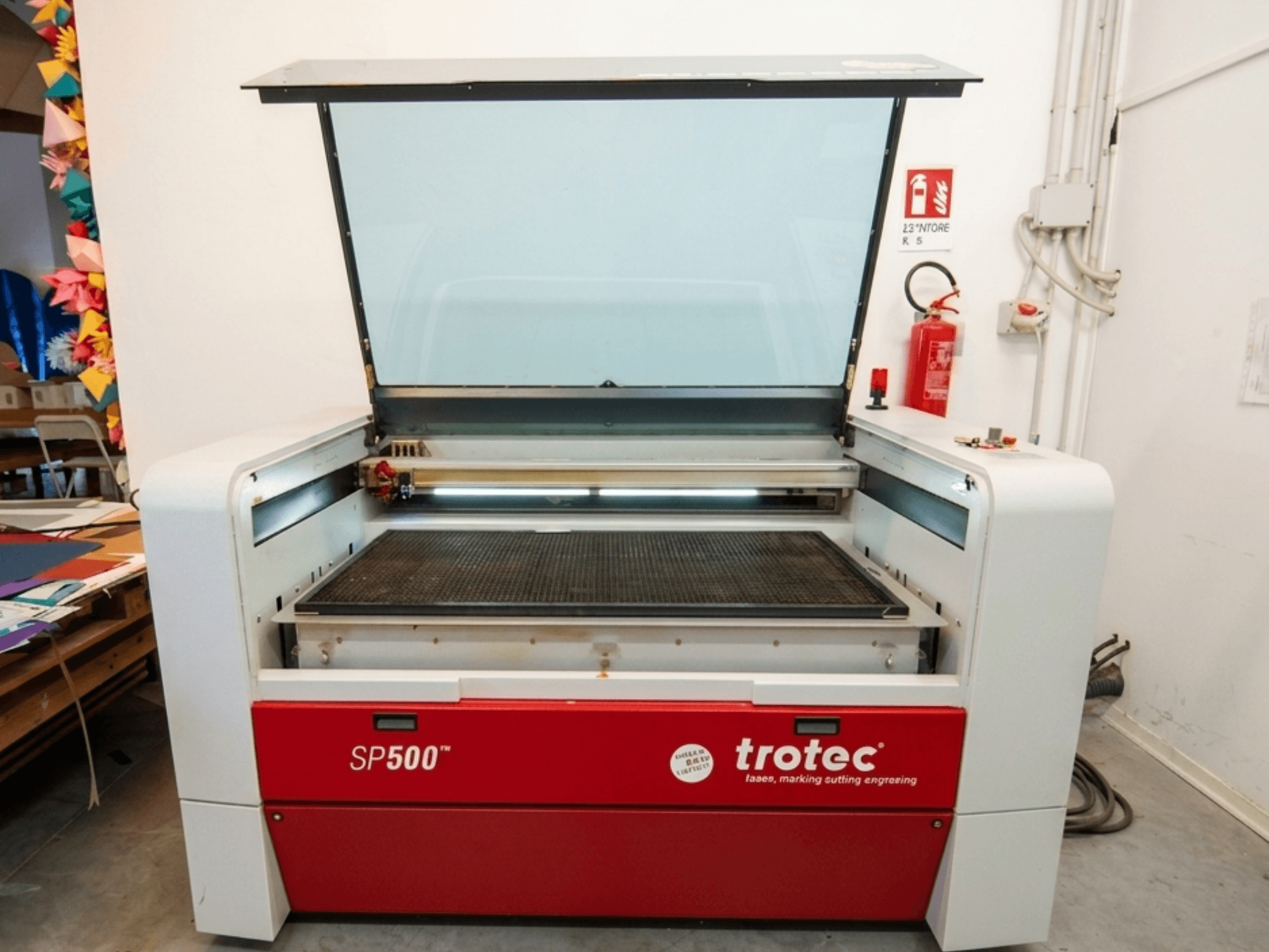Trotec SP500 C200 lazerinio graviravimo staklių vaizdas iš priekio, atidarytu dangčiu, kuriame matoma darbo zona ir valdikliai.