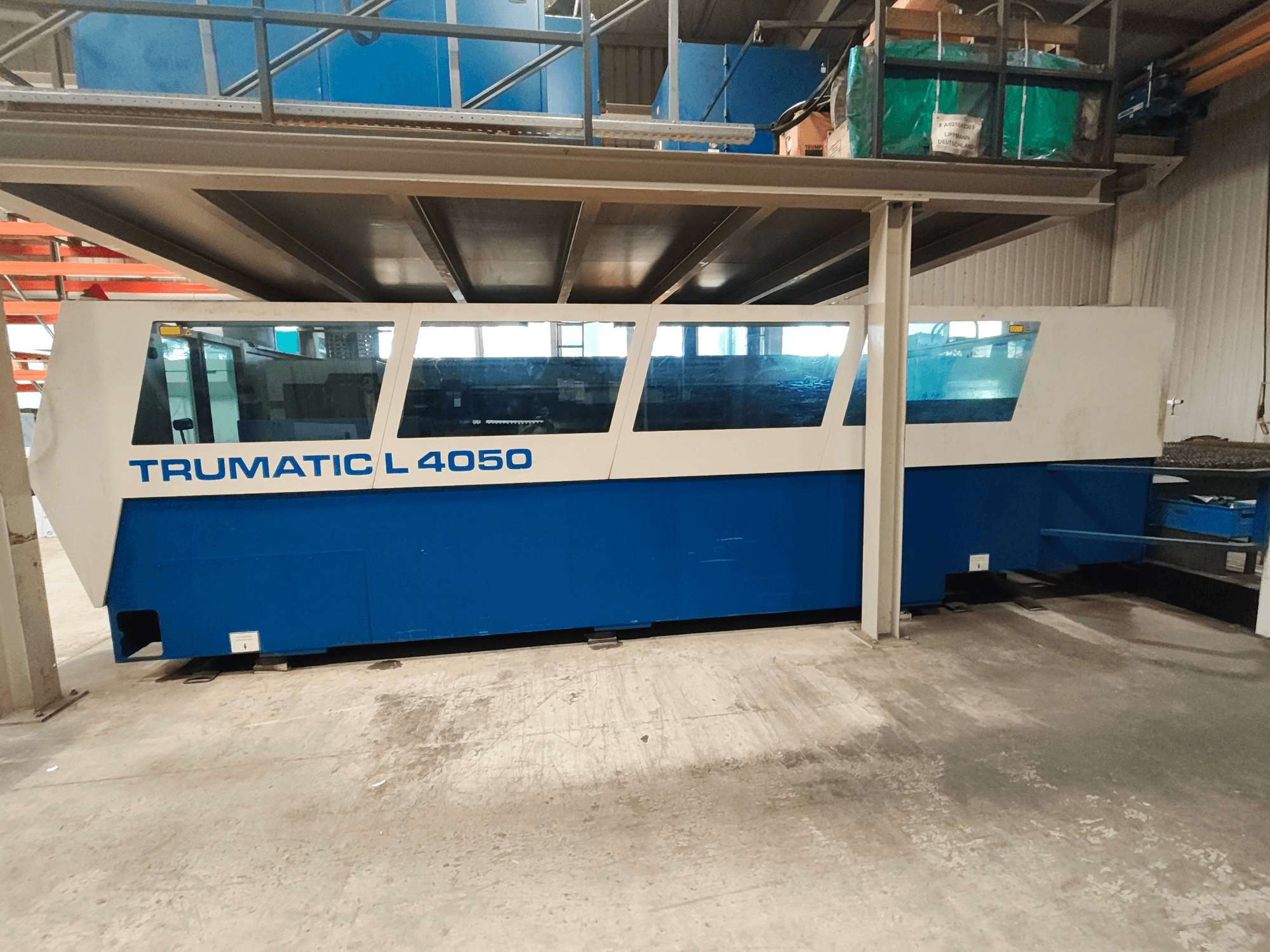 CO₂ lazerinio pjovimo staklės „TRUMPF TruLaser 450“ iš šono, mėlynos ir baltos spalvų, su matomu valdymo skydeliu ir darbo zona.
